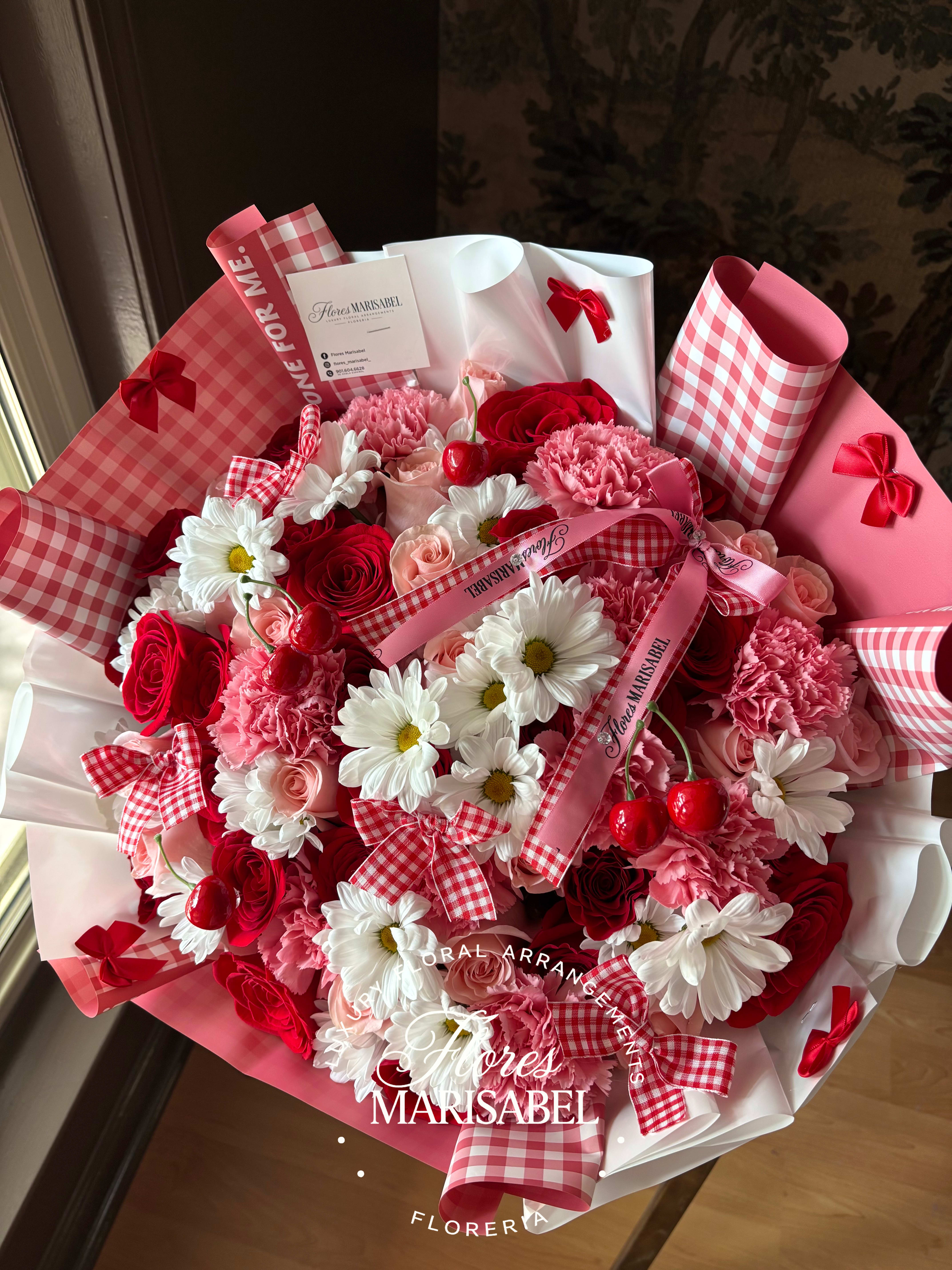 Pink and red bouquet with roses, carnations, and daisies wrapped in gingham paper