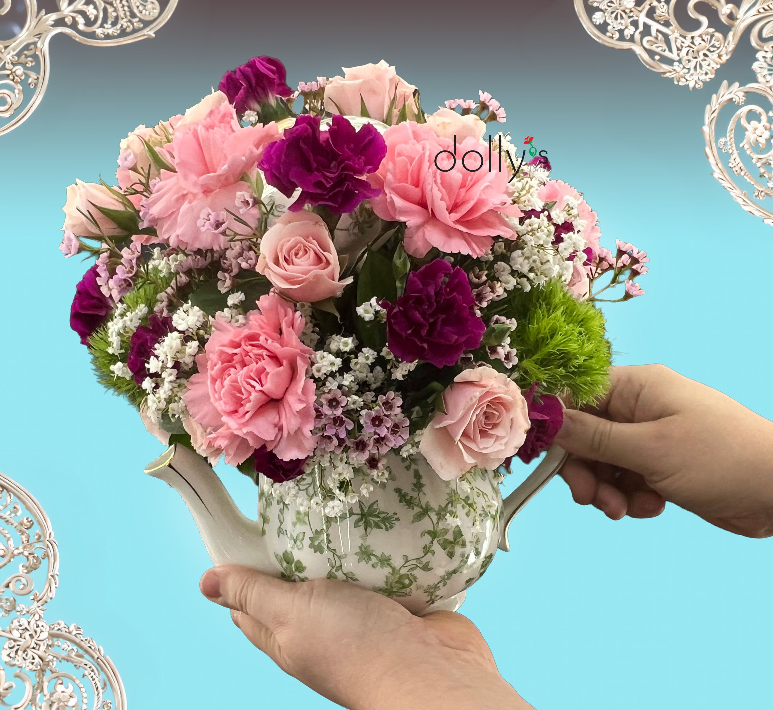 Lady Violet  - A dense, rounded cluster of blush and deep purple blooms arranged in a vintage-style ceramic teapot vase makes a cheerful, feminine centerpiece perfect for a birthday, Mother's Day, or just because. Lady Violet blends ruffled pink carnations and soft pink spray roses with jewel-toned purple flowers and small white filler blossoms so the person you're thinking of will feel both seen and celebrated the moment they walk in the door.  The arrangement sits in a white ceramic teapot (and in some versions a matching ceramic dish) with a green floral pattern, giving it a whimsical, gift-ready look that doubles as keepsake décor. Bright green accent blooms and dianthus add texture and contrast to the layered palette of pink, purple, white, and fresh greenery; the compact, all-around composition works equally well on a side table, kitchen island, or as a polished centerpiece.  Ideal for housewarming, thank-you gestures, thinking-of-you moments, Best Friends Day, or a gentle "I'm sorry," Lady Violet arrives ready to make someone's day brighter. Order as a sweet spring surprise or year-round pick-me-up; the teapot vase is reusable and the flowers are arranged for full visual impact from every angle.