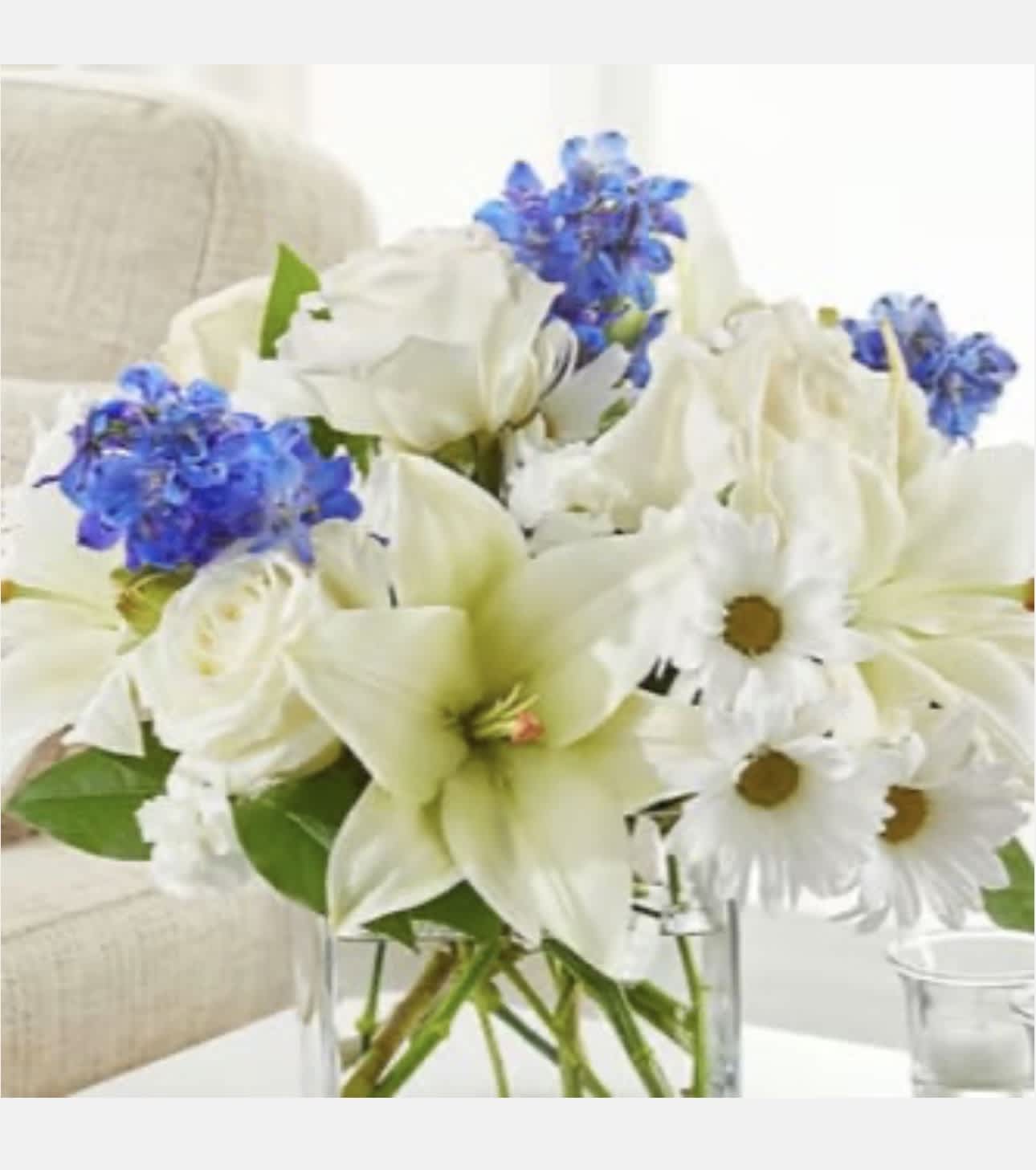 White lilies, daisies, and blue flowers in a clear glass vase