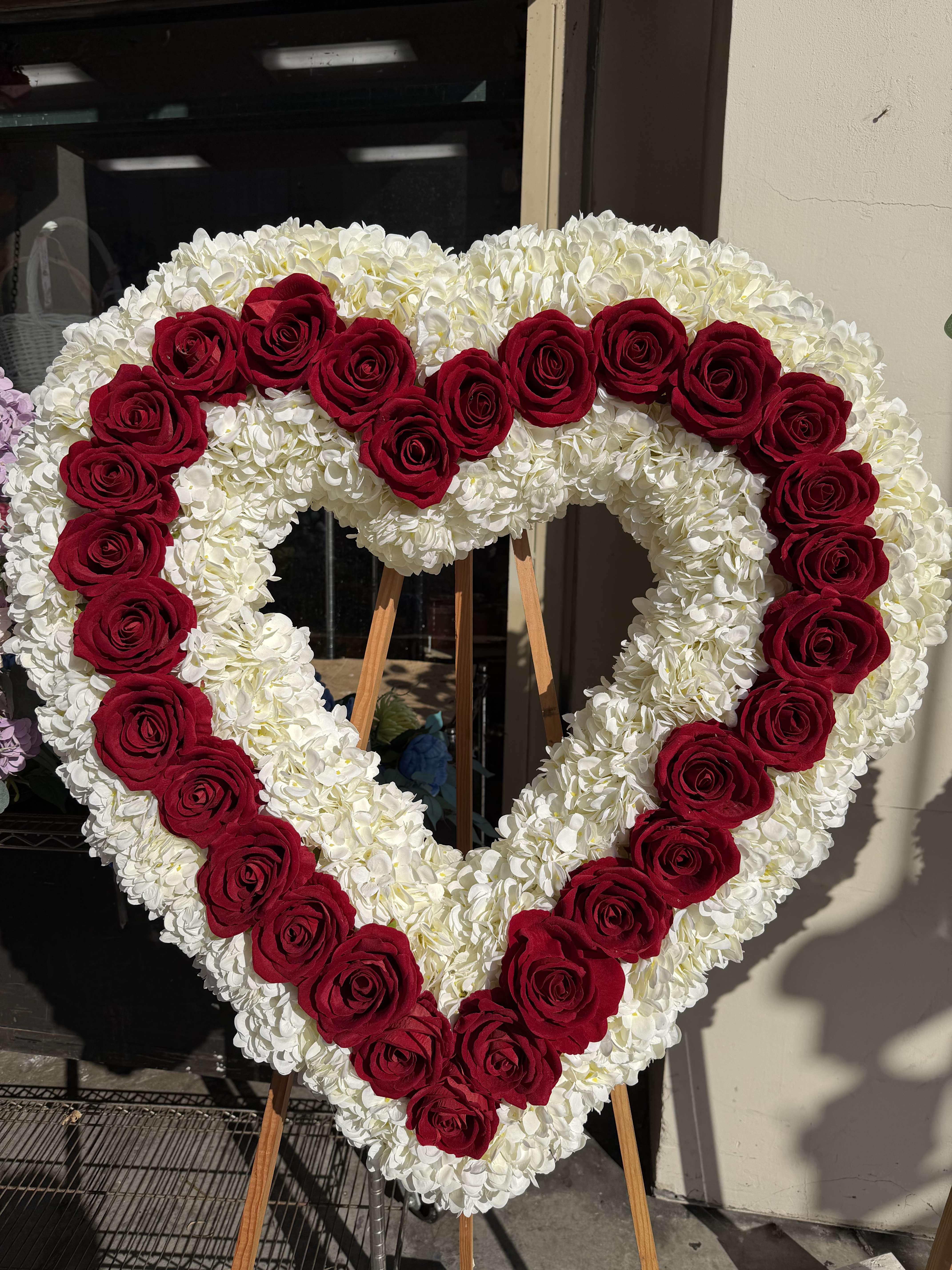 Heart-shaped floral wreath of red roses and white flowers on an easel