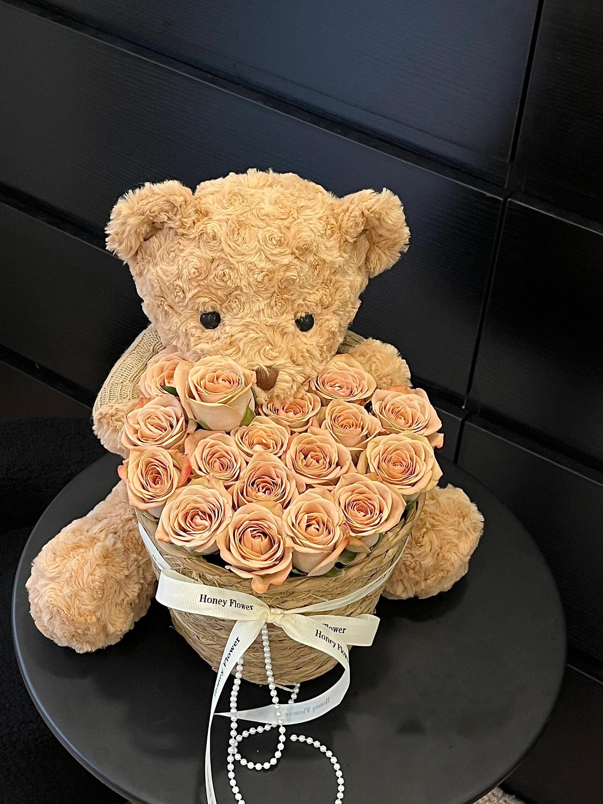 Teddy bear holding a heart-shaped box of peach roses