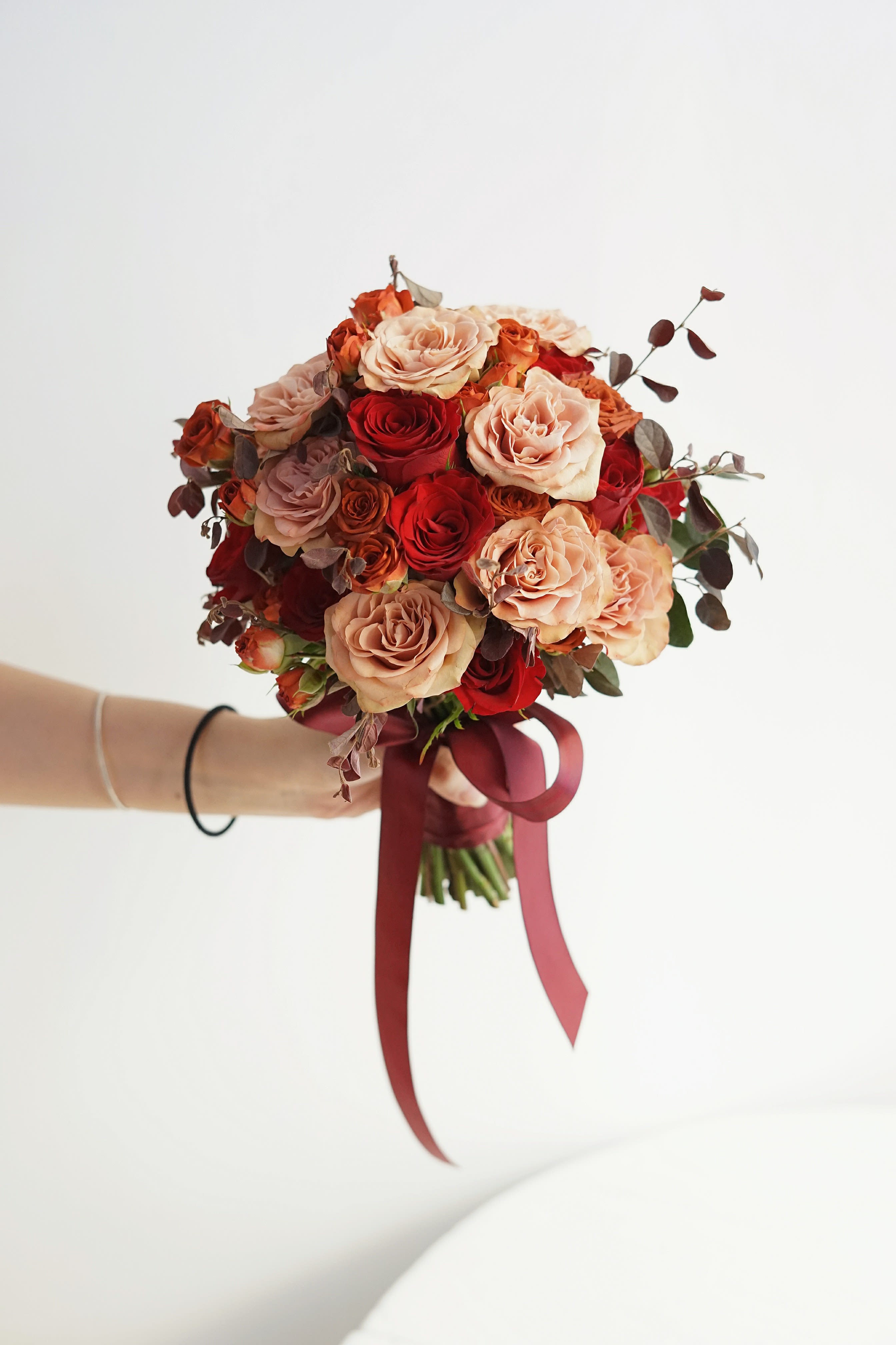 Handheld bouquet of red and blush roses tied with a burgundy ribbon