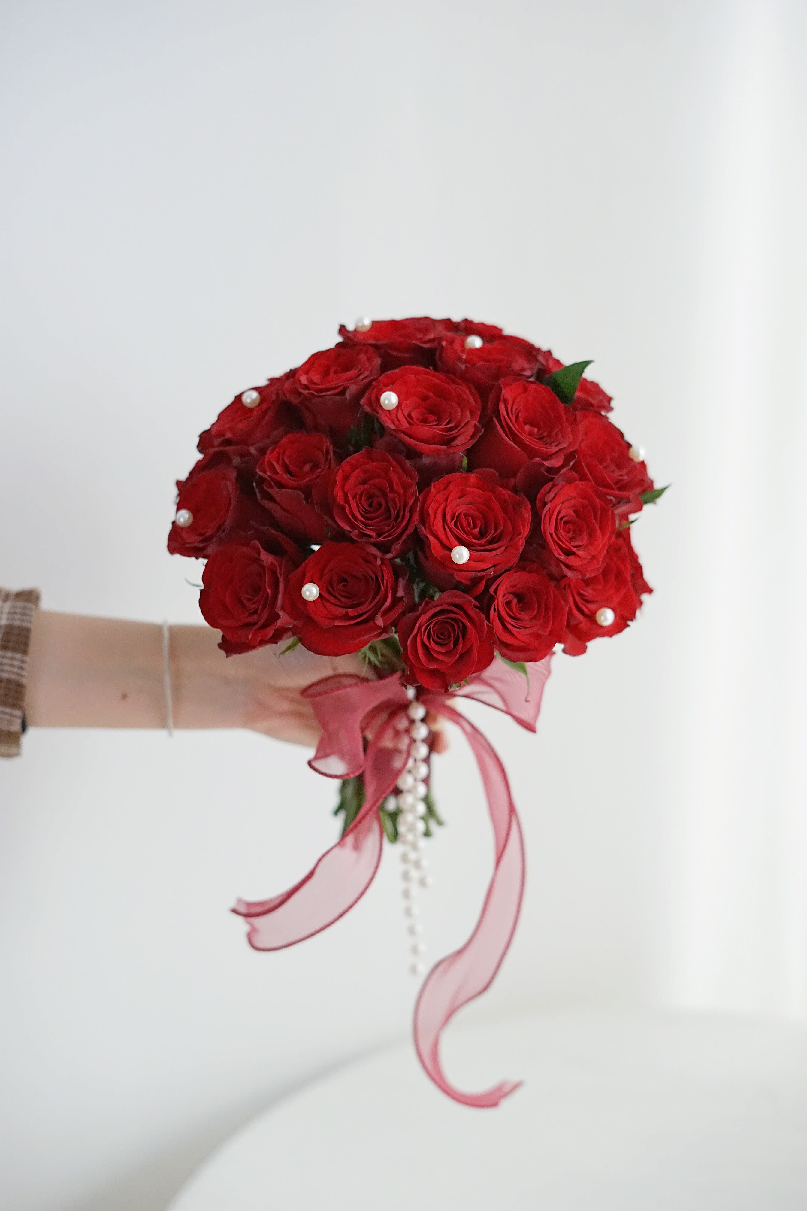 Handheld bouquet of red roses with pink ribbon and pearl accents