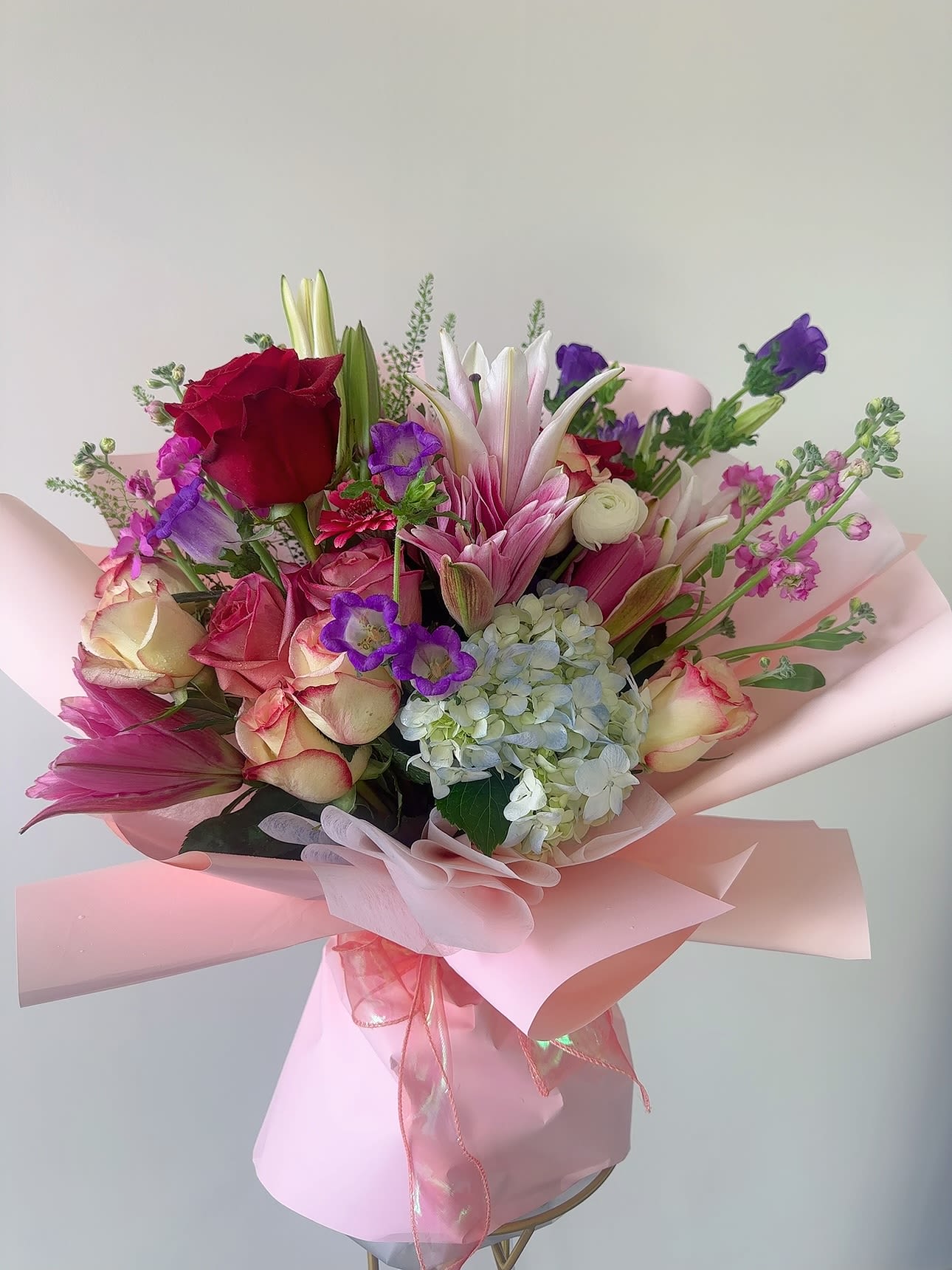 Pink and purple bouquet with roses, lilies, and hydrangea wrapped in pink paper
