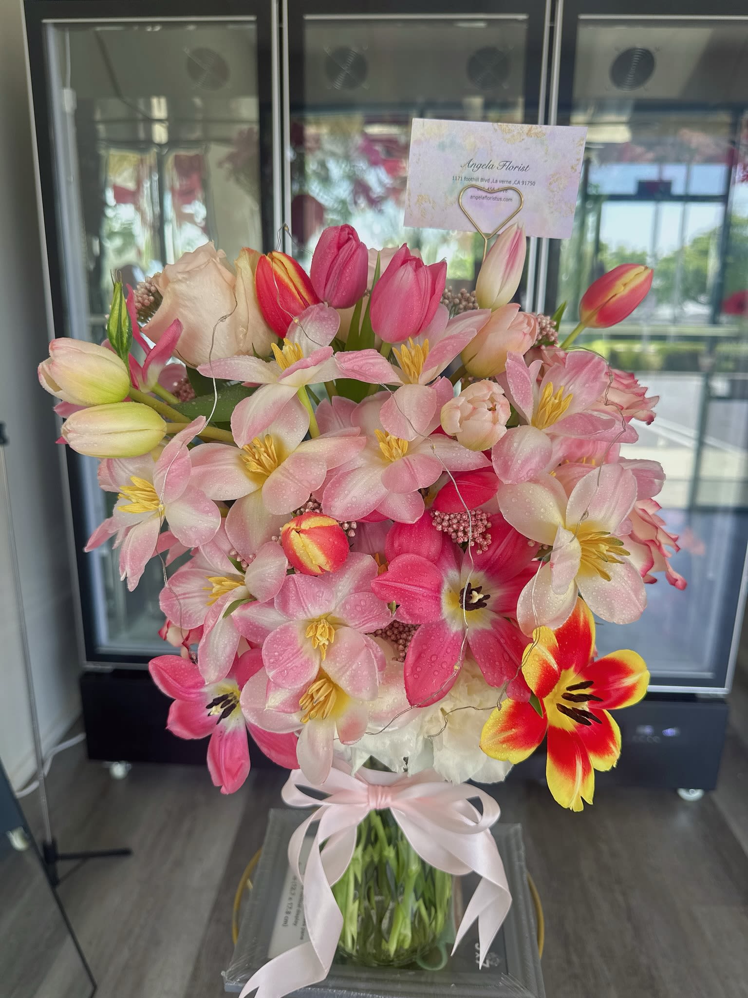 Pink and white tulips with pale blossoms in a glass vase tied with a ribbon