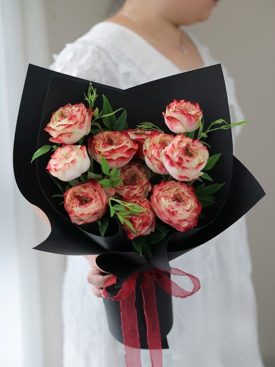 Bouquet of pink-and-cream roses wrapped in black paper with a red ribbon