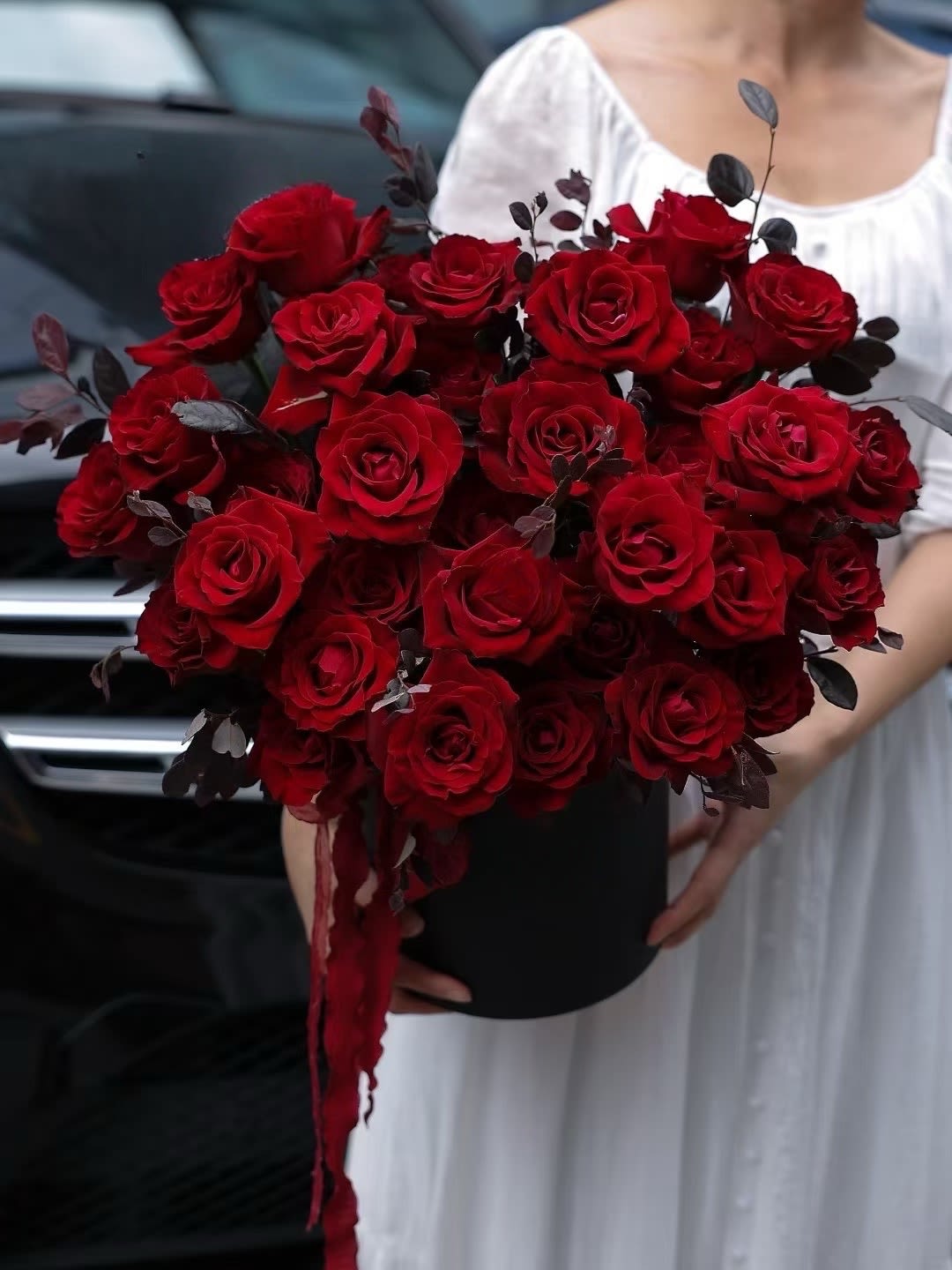 Bouquet of red roses in a black box with dark foliage