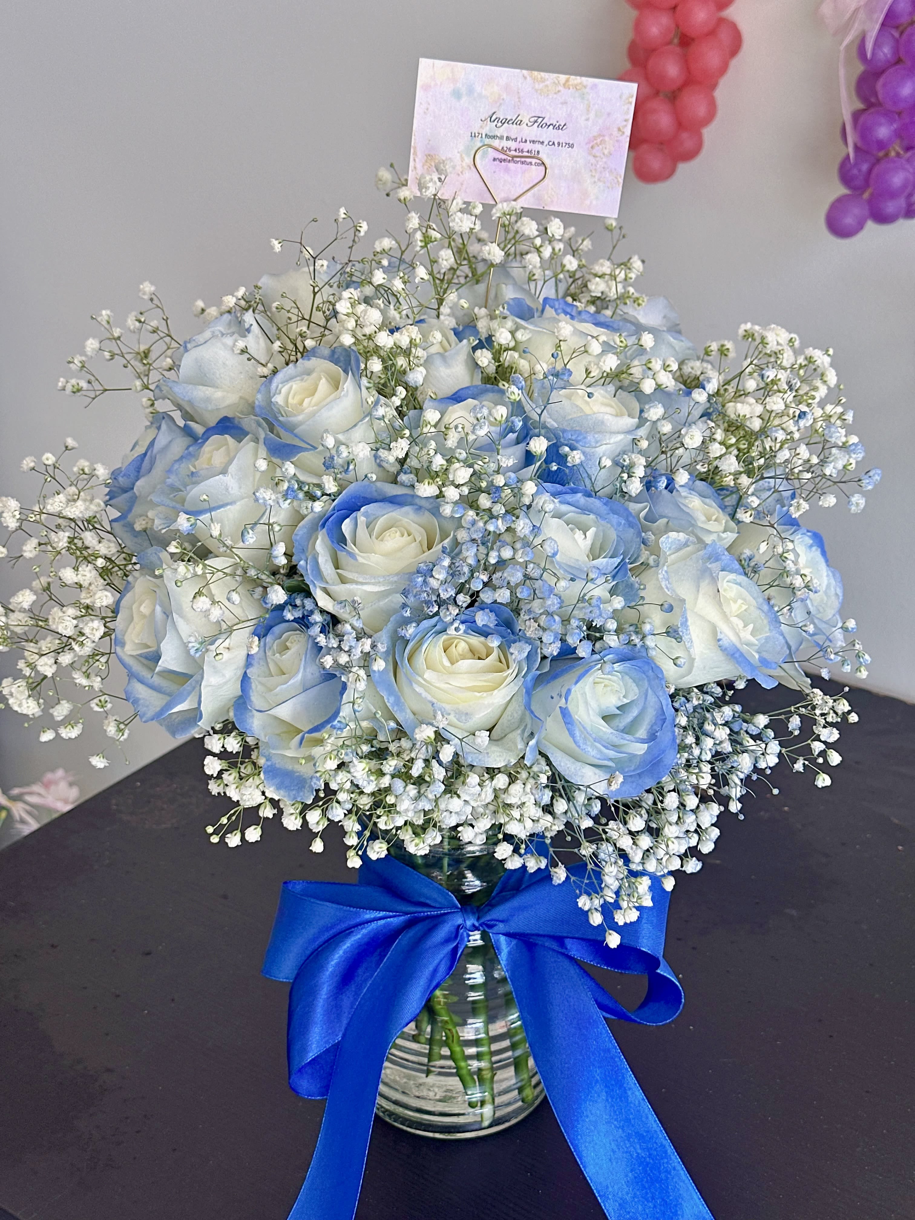 Blue-tinted white rose bouquet in a glass vase with baby's breath and a blue ribbon