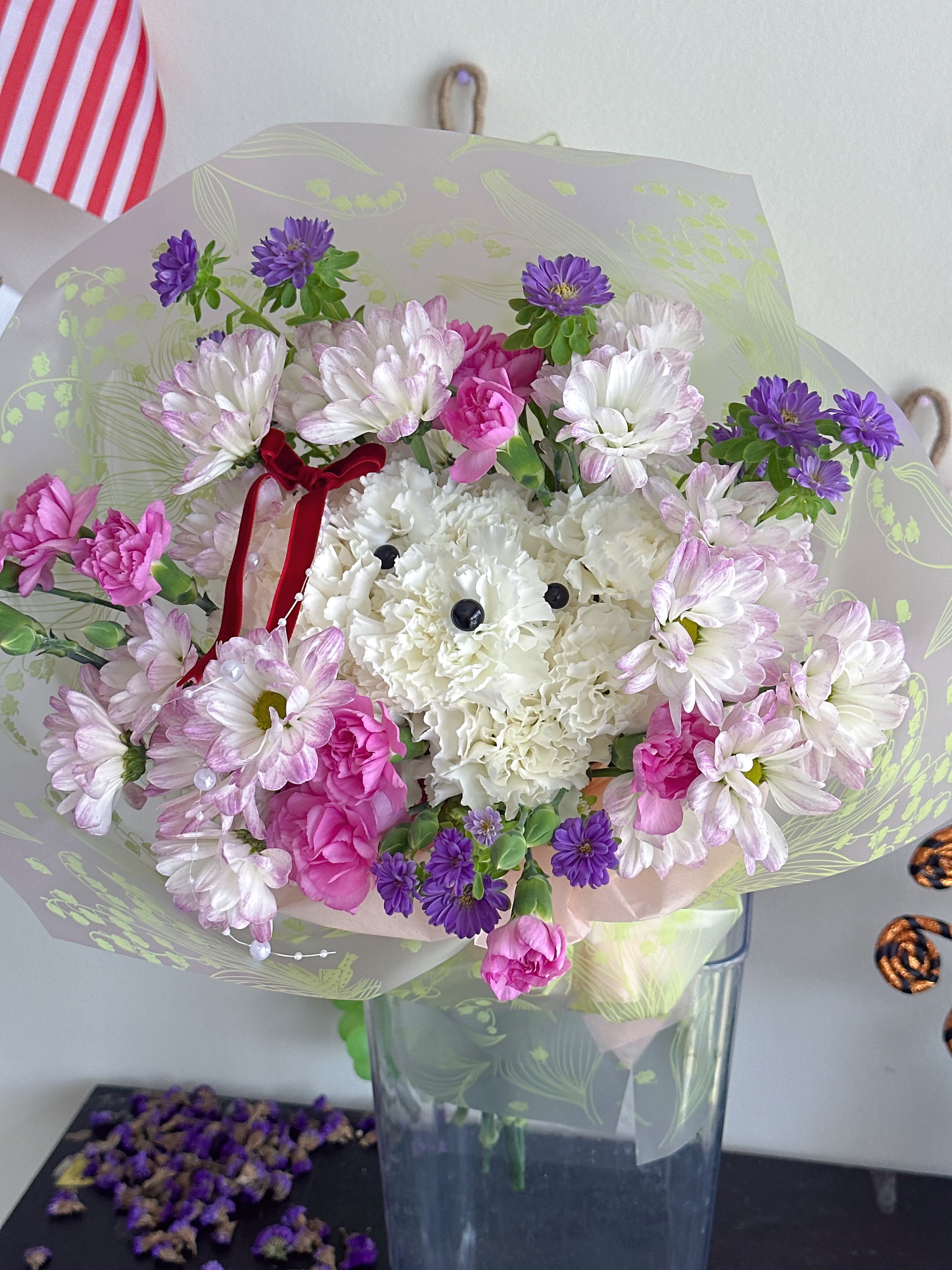 Bouquet of white, pink, and purple flowers in clear wrap with a red ribbon