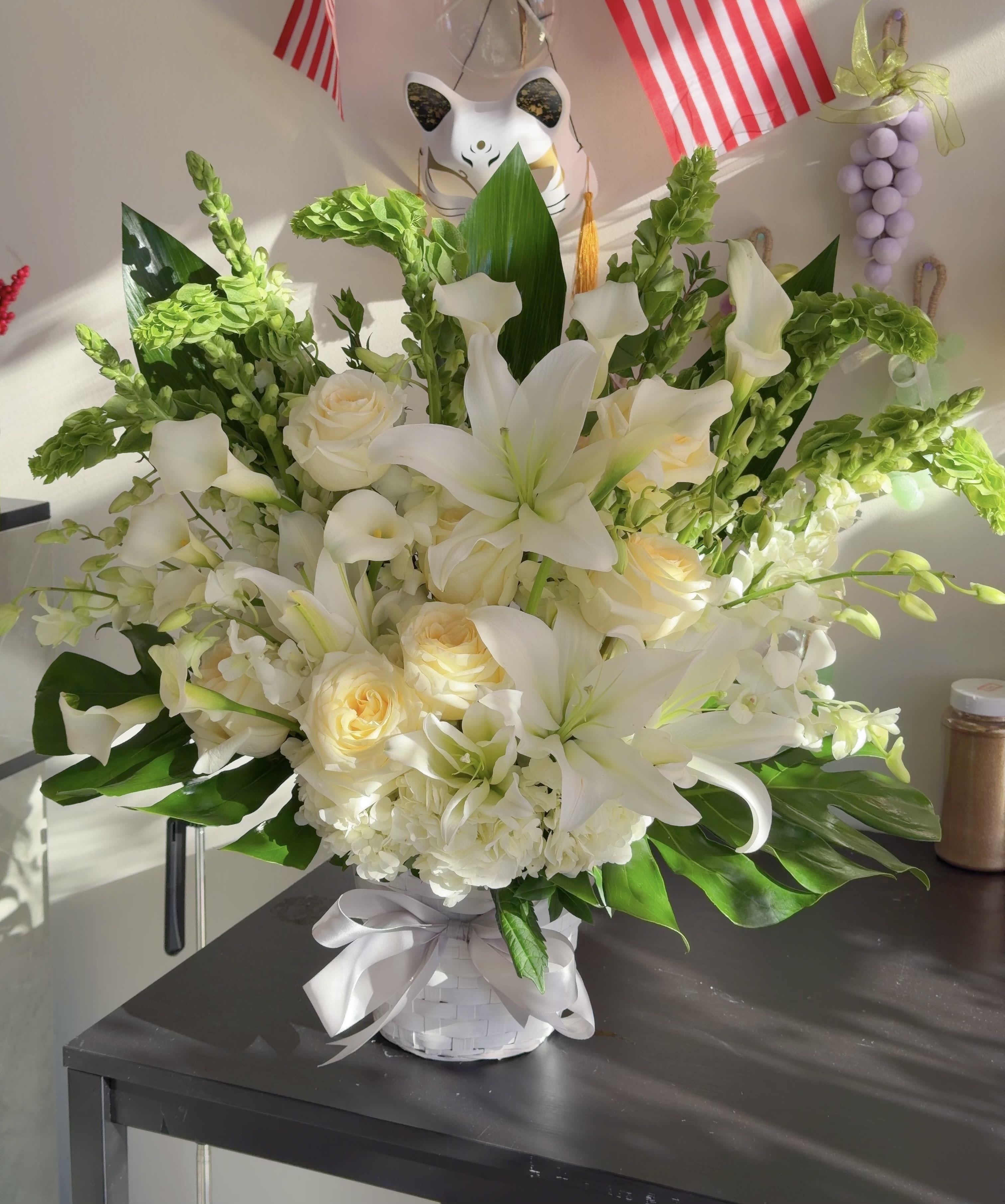 White lilies and cream roses in a white basket with a ribbon