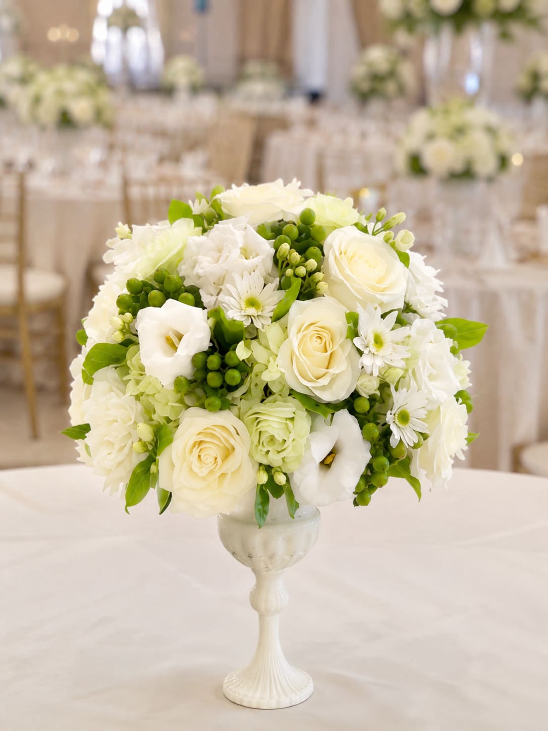 White floral arrangement in a pedestal vase with green accents
