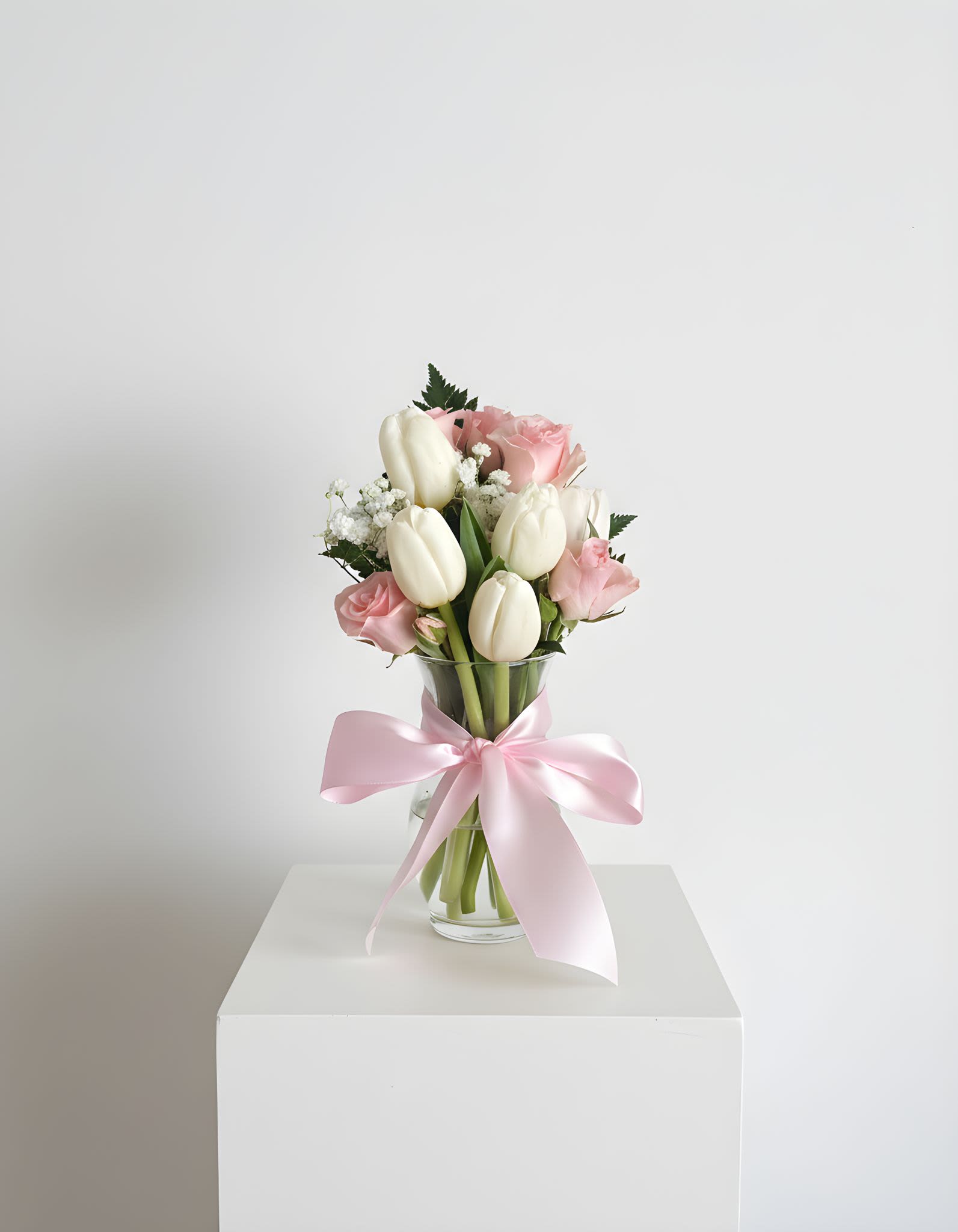 Pink roses and white tulips in a glass vase with a pink ribbon
