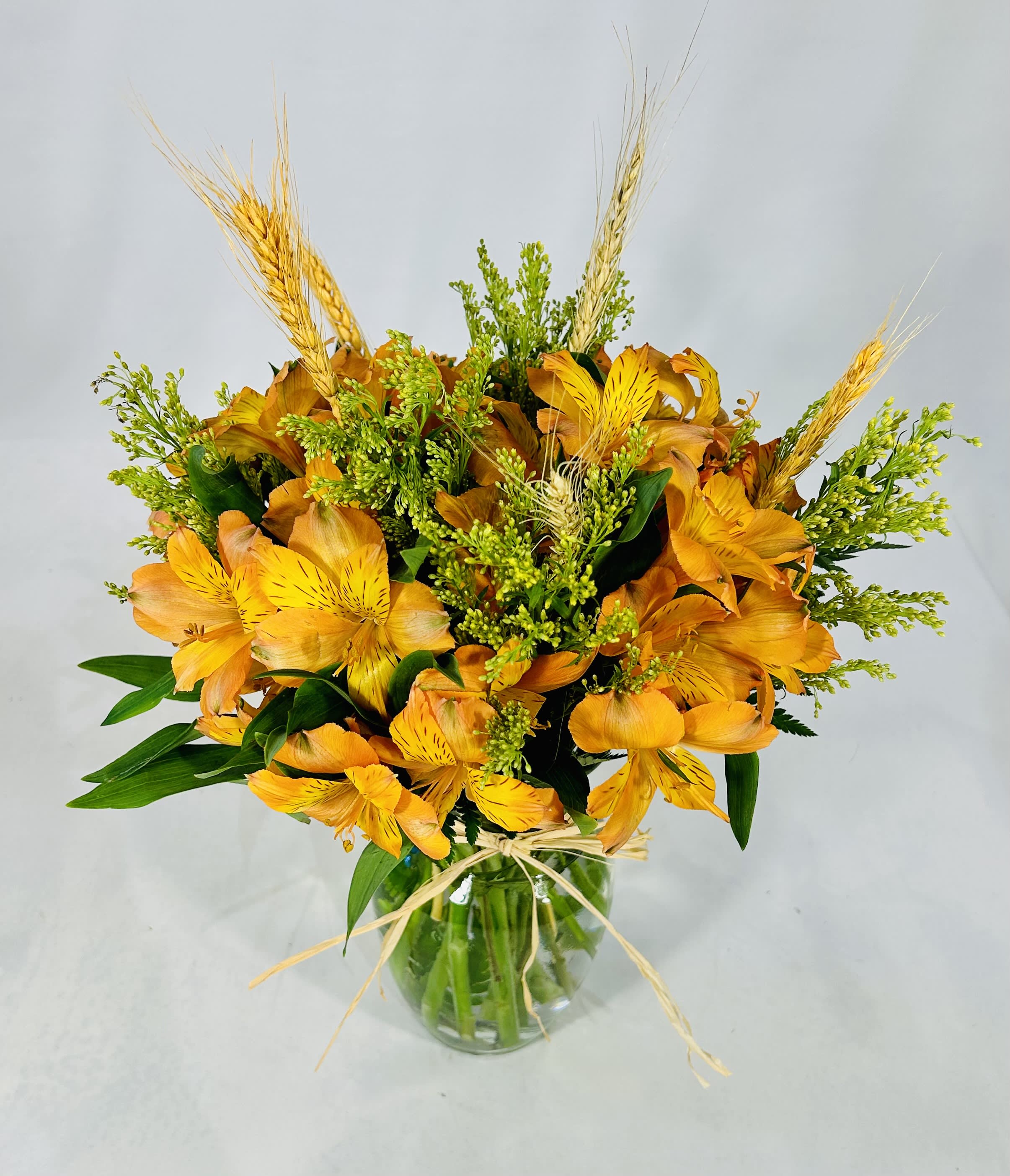 Orange alstroemeria bouquet in a clear glass vase with wheat accents