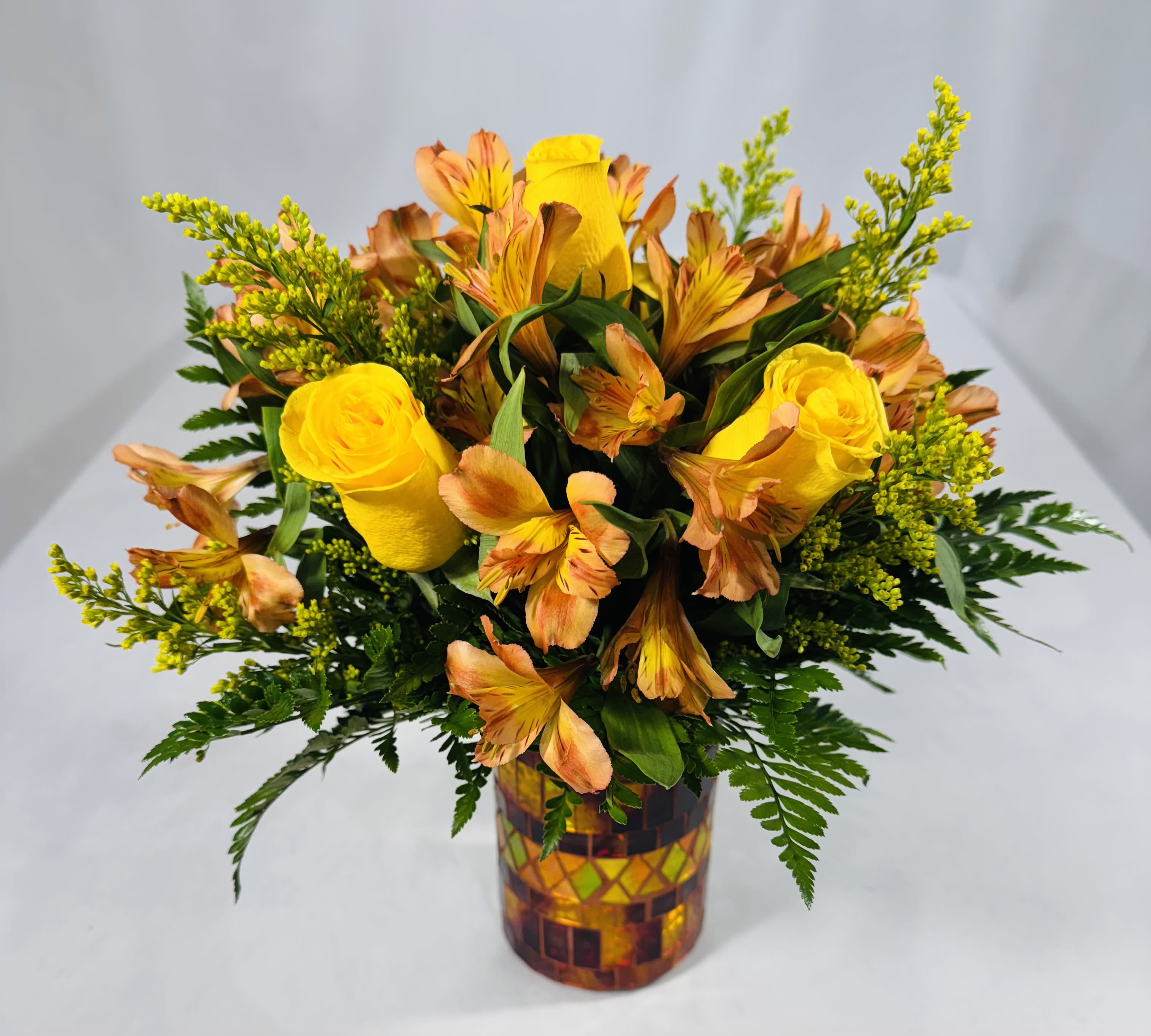 Yellow roses and orange alstroemeria in a mosaic glass vase.