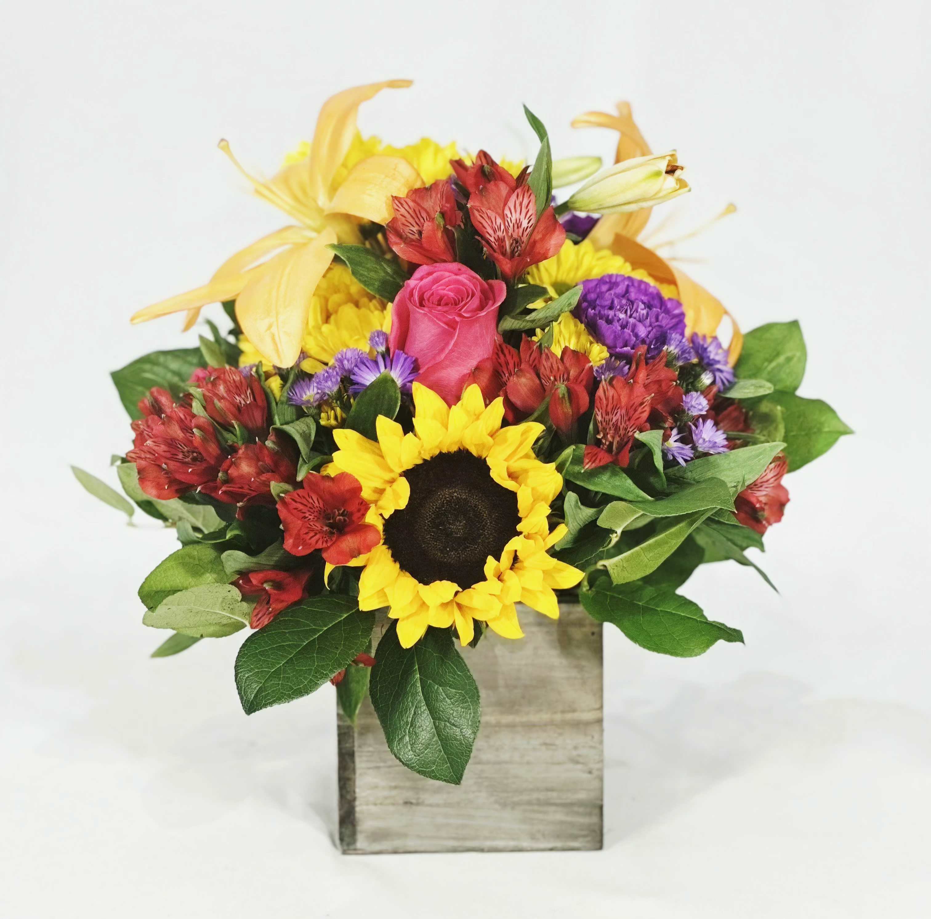 Mixed bouquet with a sunflower, pink rose, and yellow lilies in a wooden box