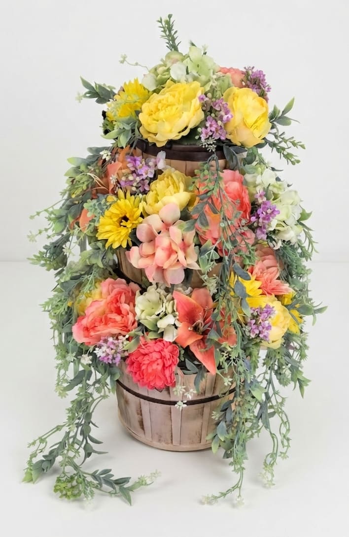 Tiered floral arrangement in a wooden basket with yellow, pink, and coral blooms