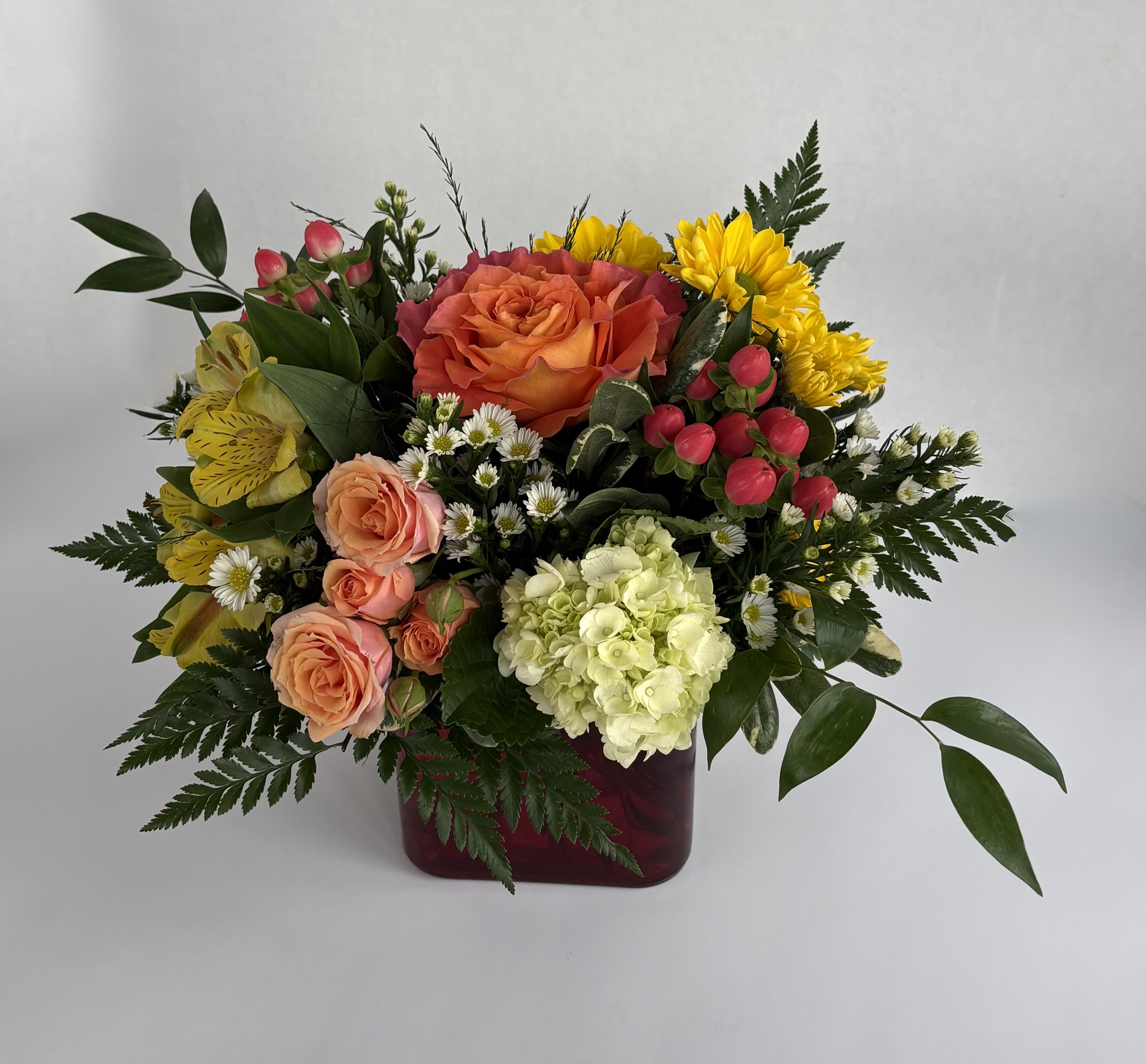 Summer Sunrise  - Summer Sunrise is designed in a red vase with summer-y hot florals. With an orange rose, yellow daisies, yellow alstromeria, peach spray roses, green hydrangea, pink hypericum, and accented with white asters. This striking bouquet brings the warmth of the sun into your home. 