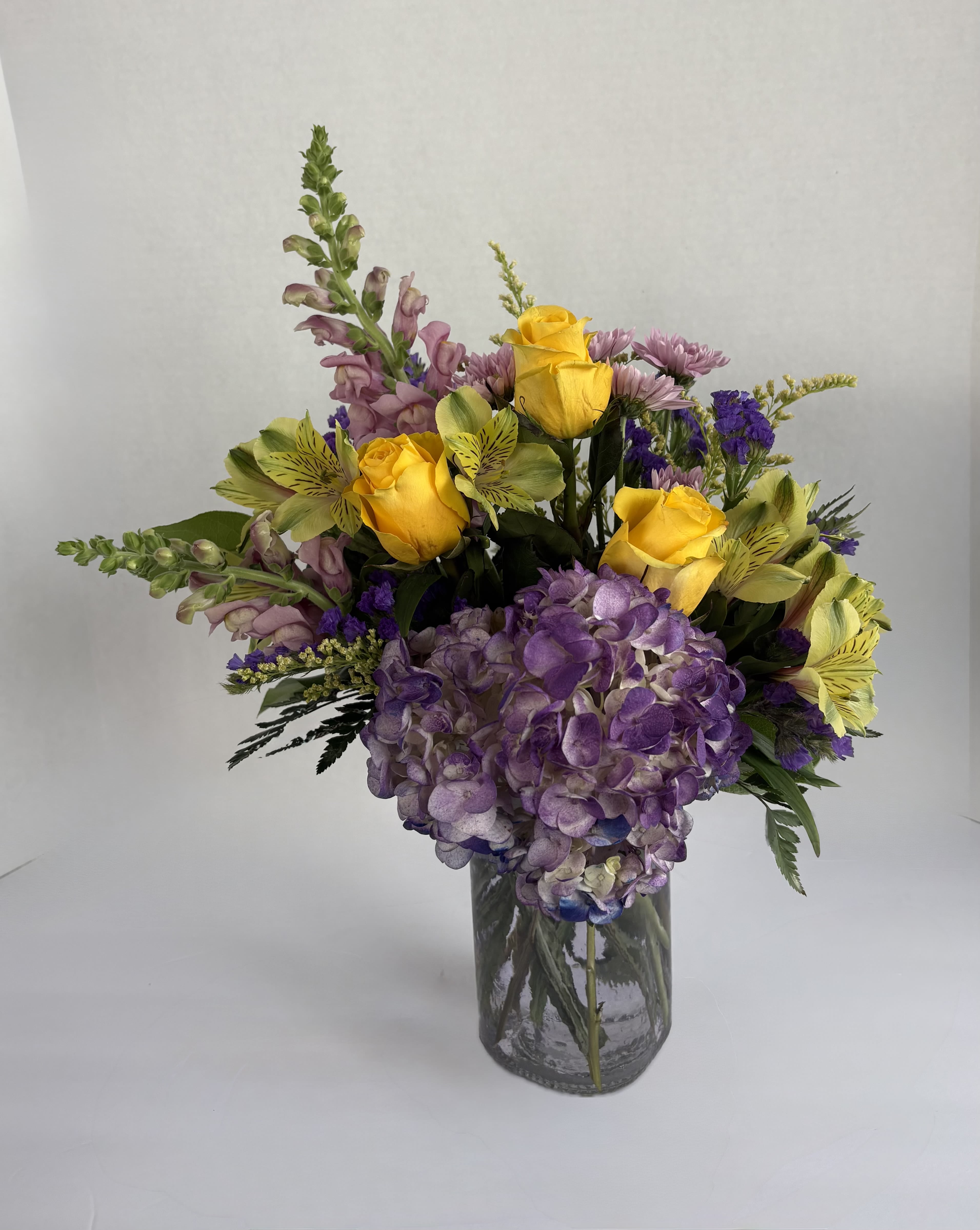 Bouquet of yellow roses, purple hydrangea, and mixed blooms in a glass vase