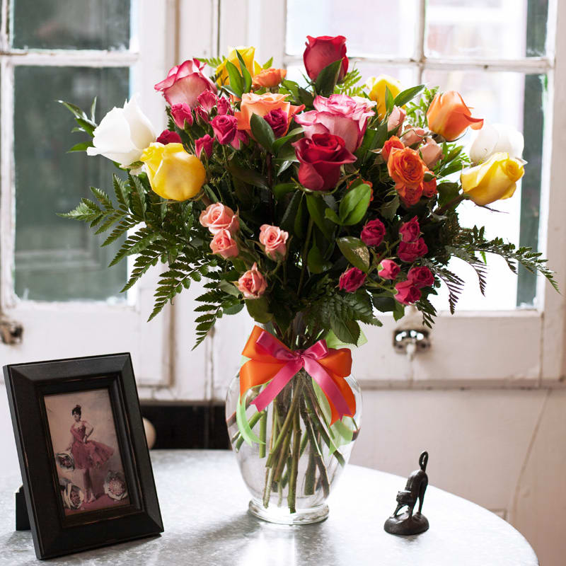 Mixed roses in a clear glass vase with a pink and orange ribbon