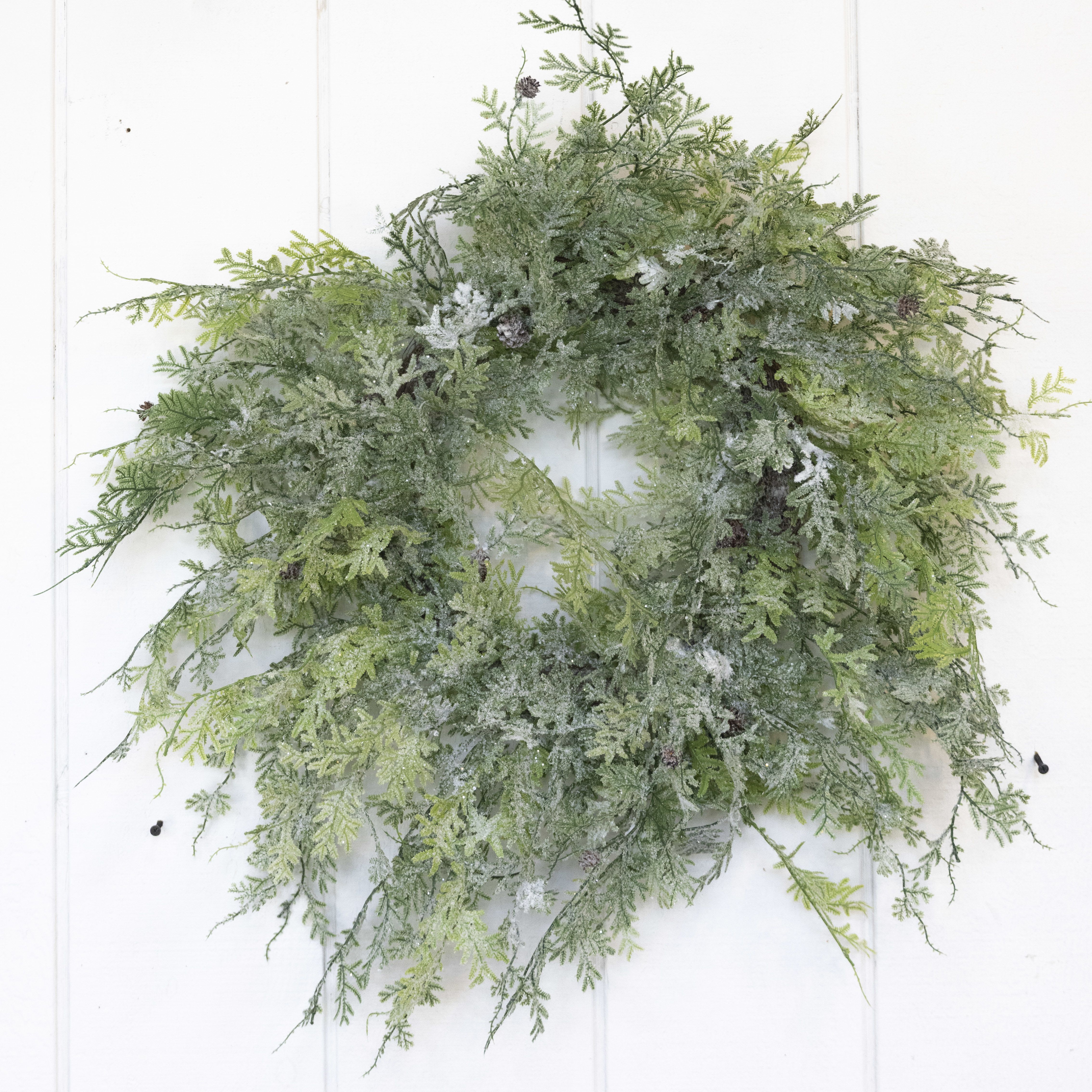 A green foliage wreath with frosted accents on a white door