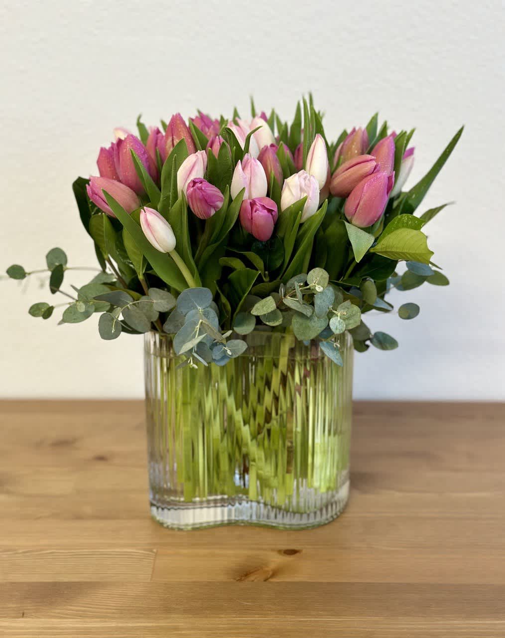 Pink tulips arranged in a clear glass vase with eucalyptus