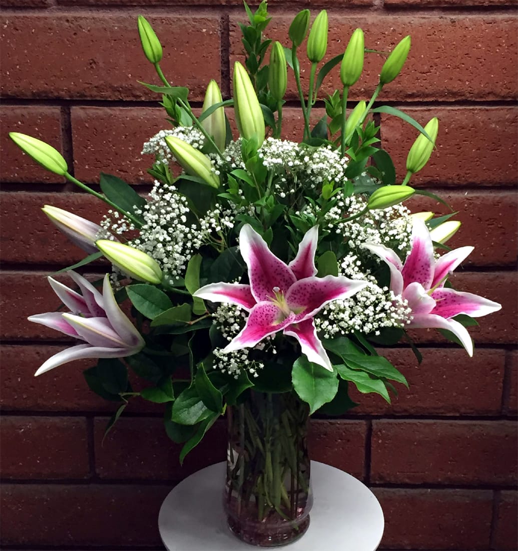 Tall glass vase of pink stargazer lilies with white baby's breath