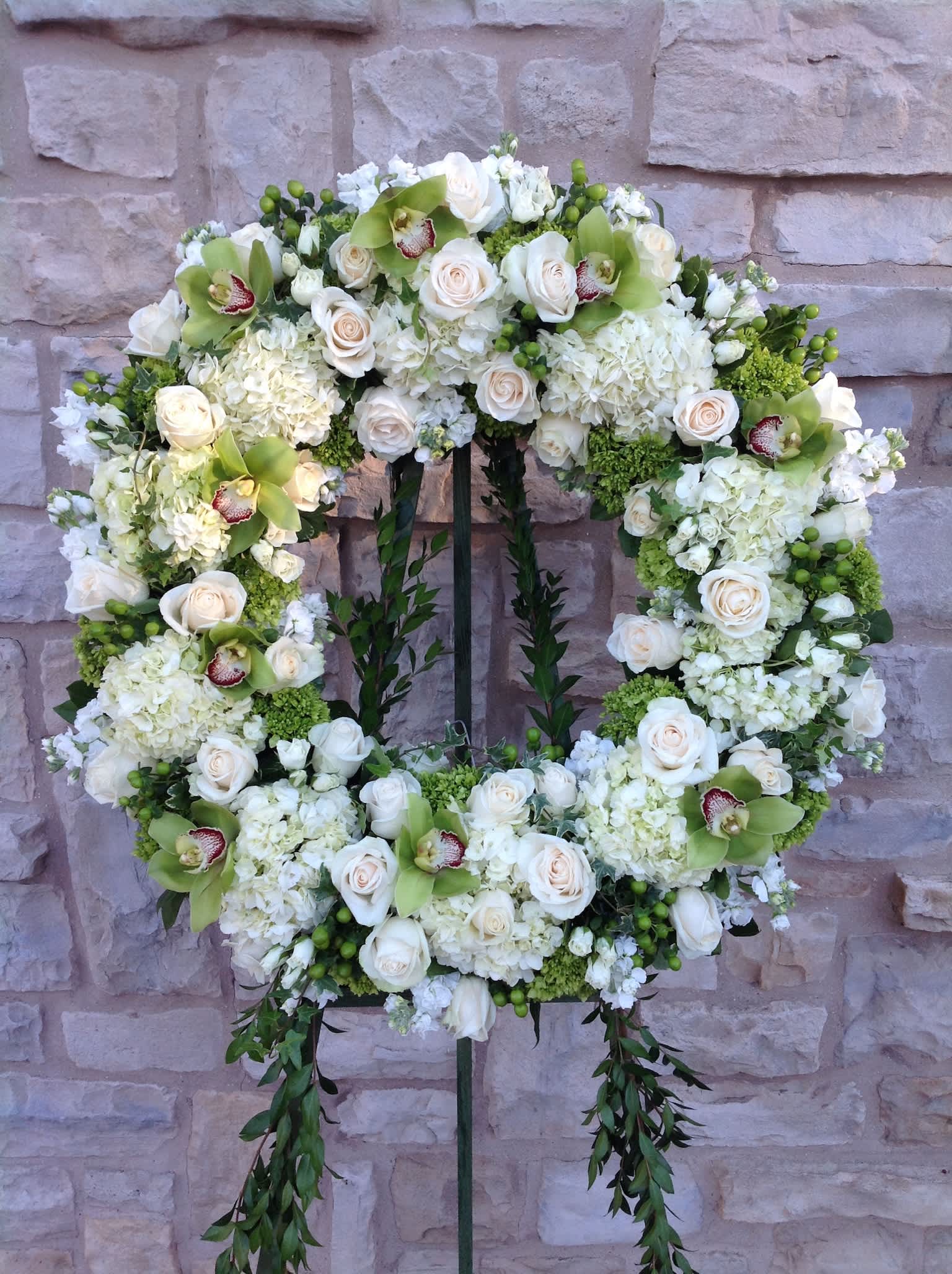 White floral wreath on a stand with roses and orchids