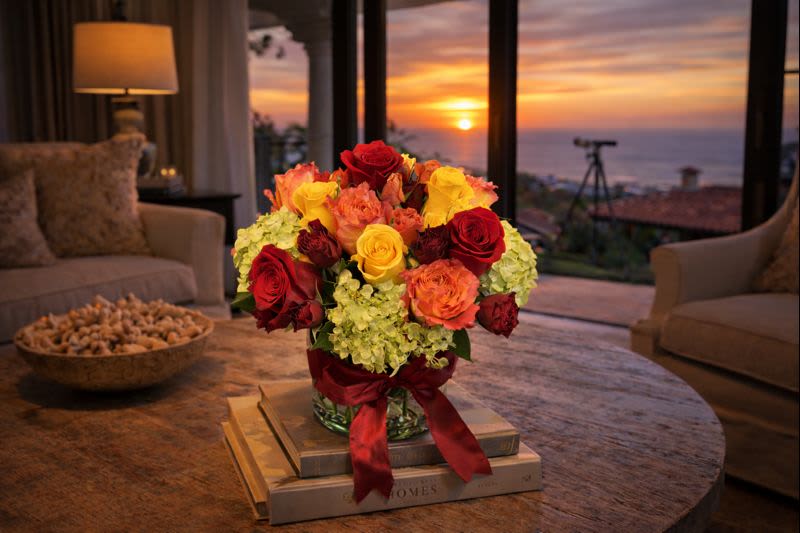 Bouquet of red, yellow, and orange roses in a glass vase with a ribbon