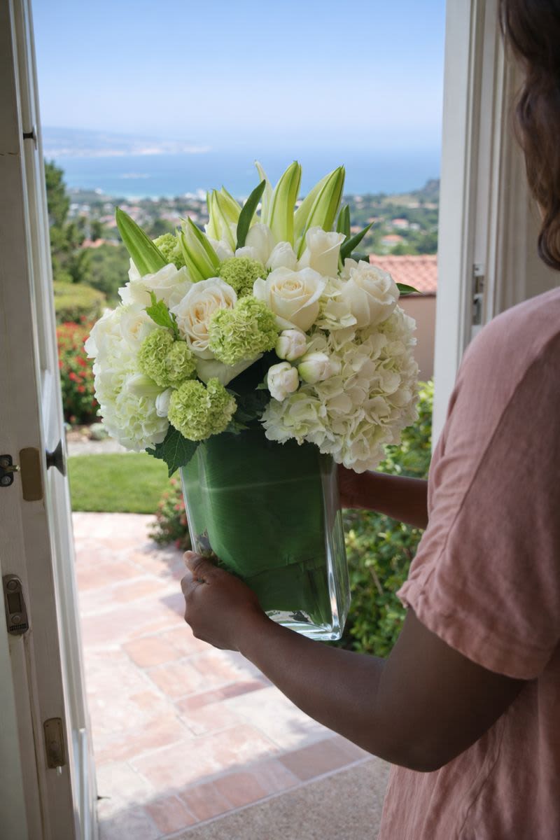White floral arrangement in a clear glass vase being held at a doorway