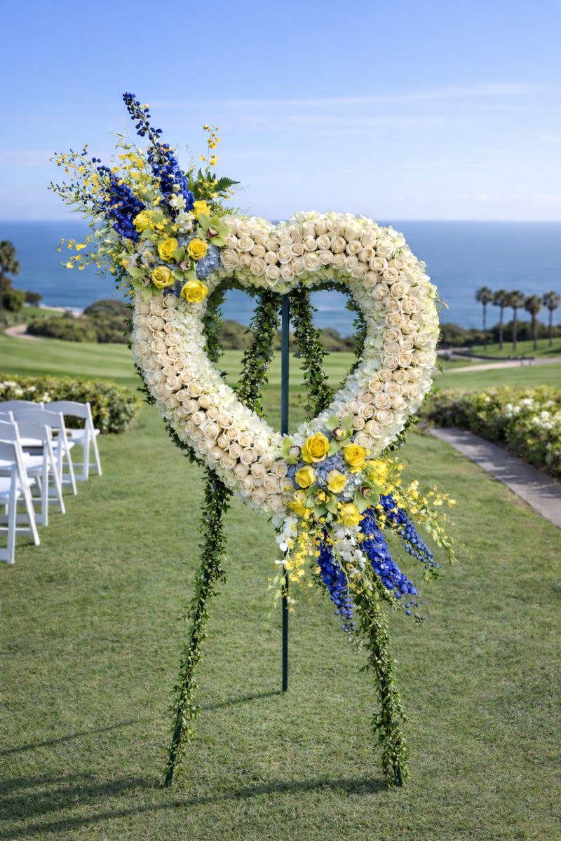 Heart-shaped floral wedding arch with white, yellow, and blue flowers