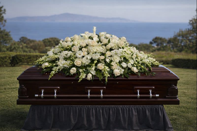 White floral casket spray on a dark wood coffin outdoors