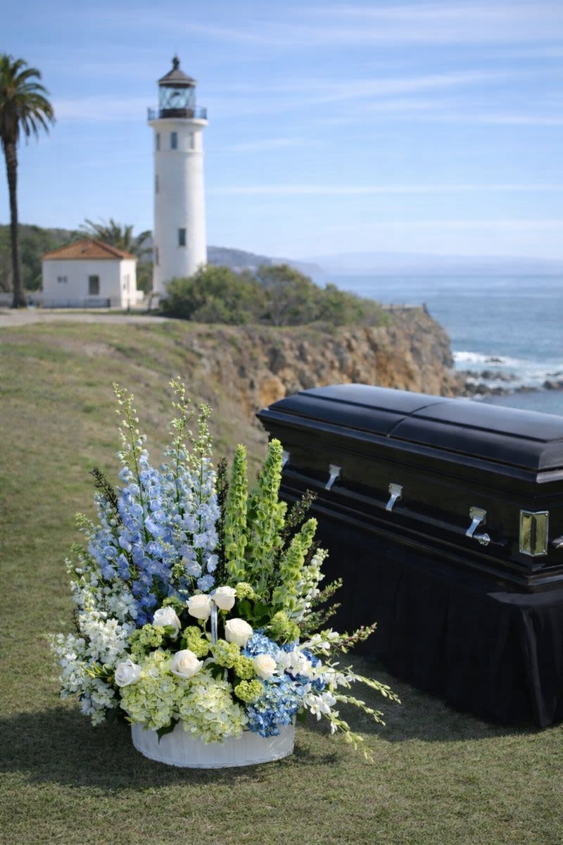 White and blue funeral flowers beside a black casket outdoors