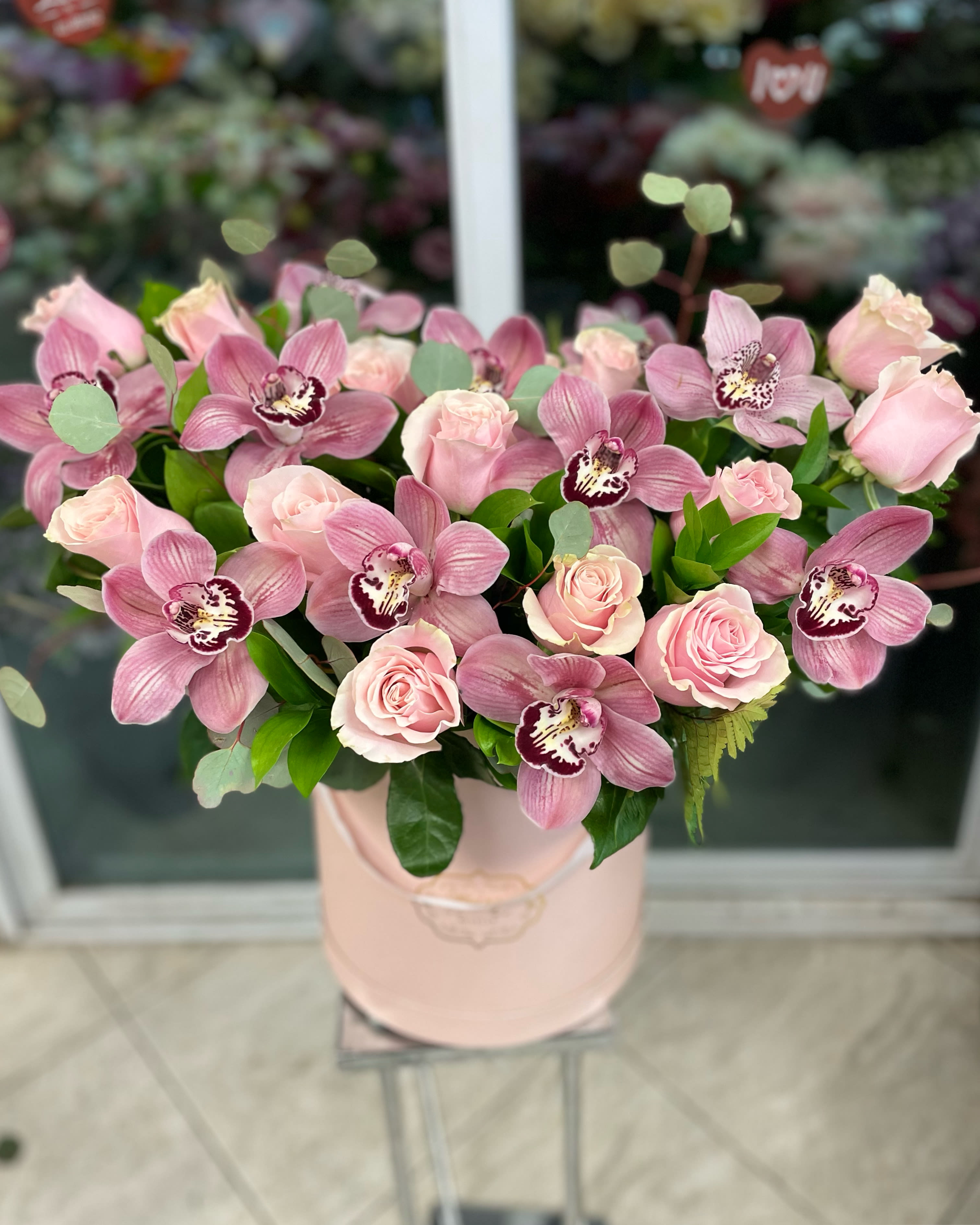 Pink roses and orchids arranged in a blush hatbox