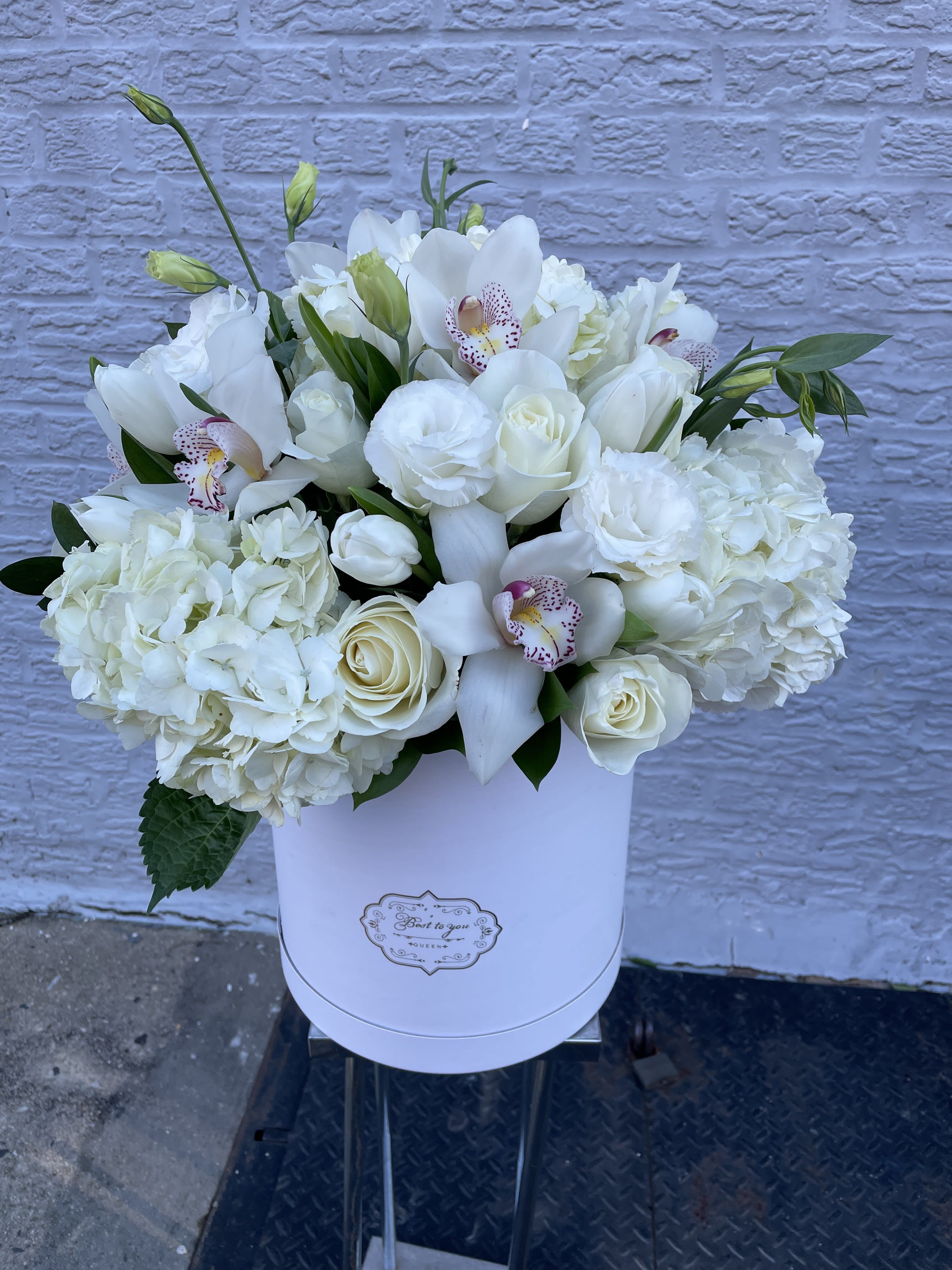 White floral arrangement in a round white box with orchids and roses