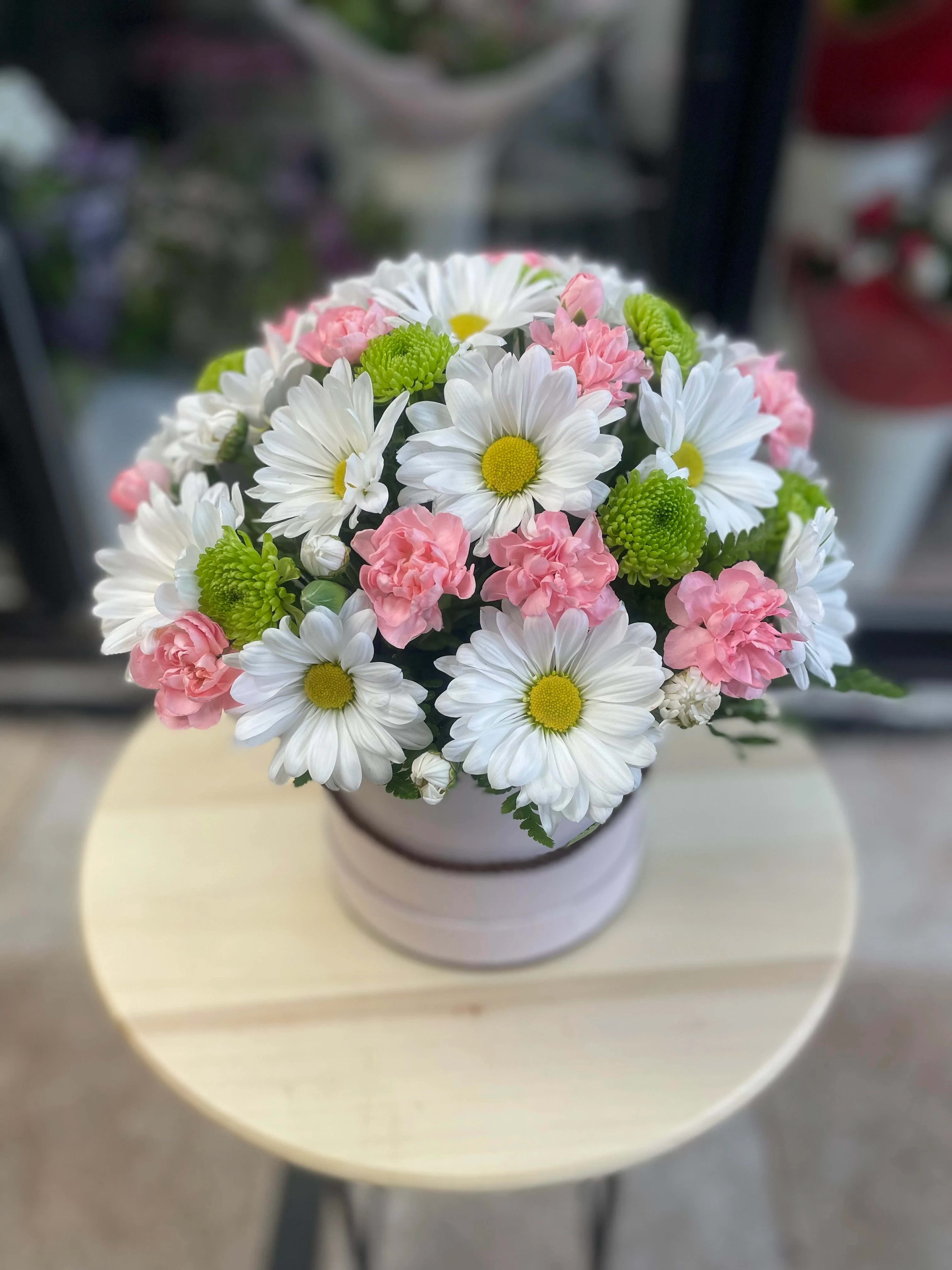Round bouquet of white daisies and pink carnations in a pale vase