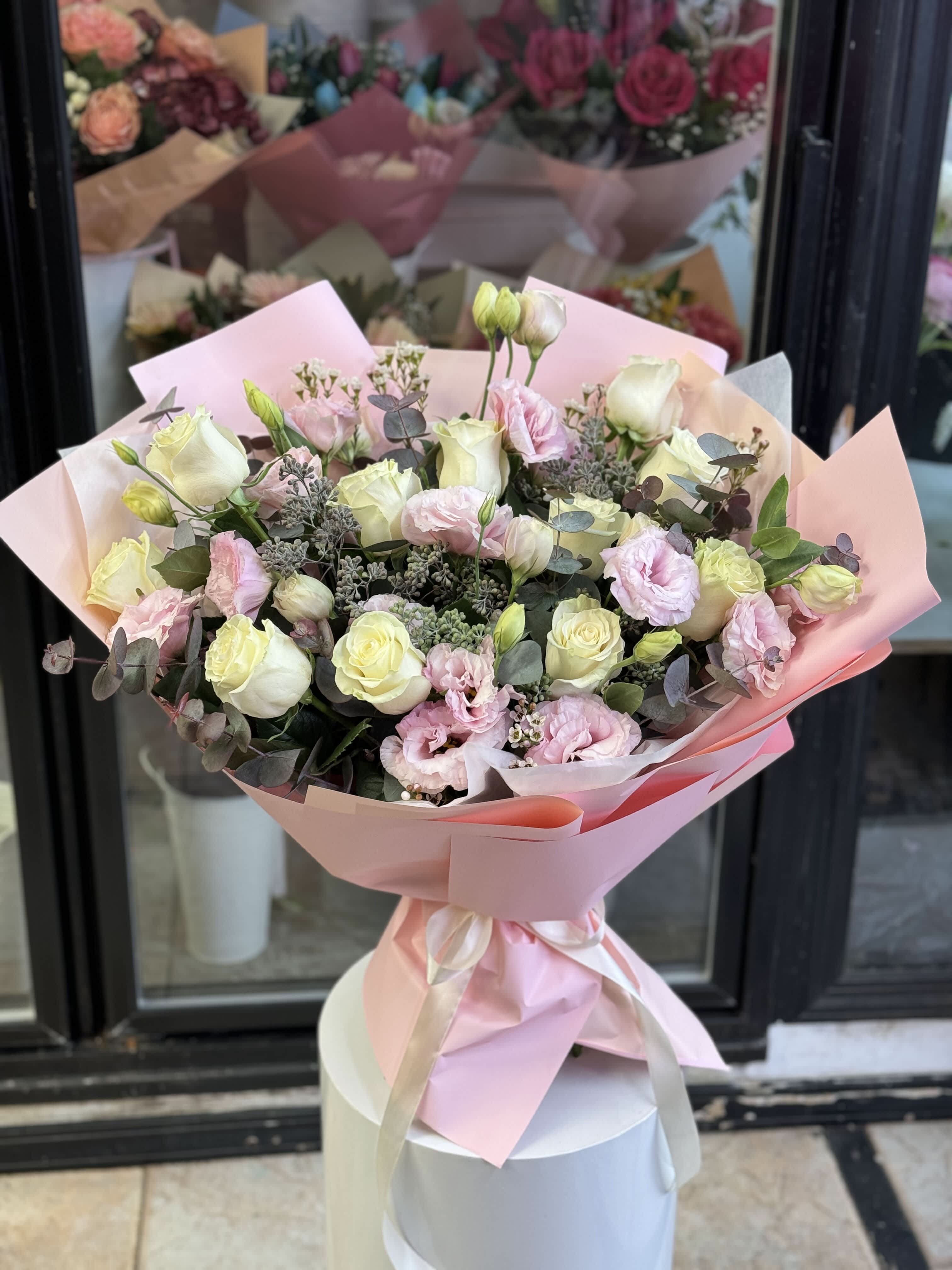 Bouquet of pale pink and cream roses with pink blooms wrapped in pink paper