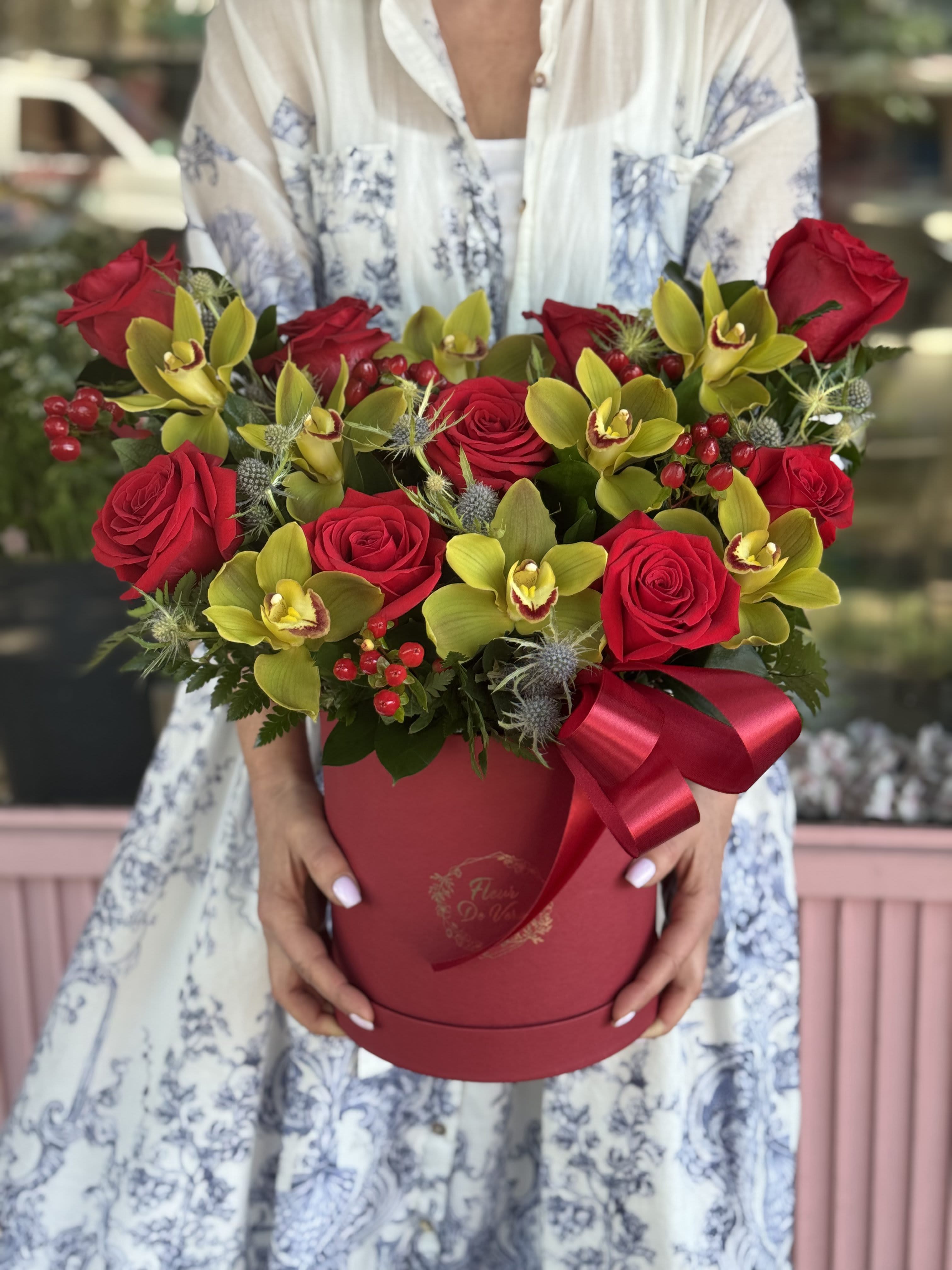 Red roses and yellow orchids arranged in a round red box with a ribbon