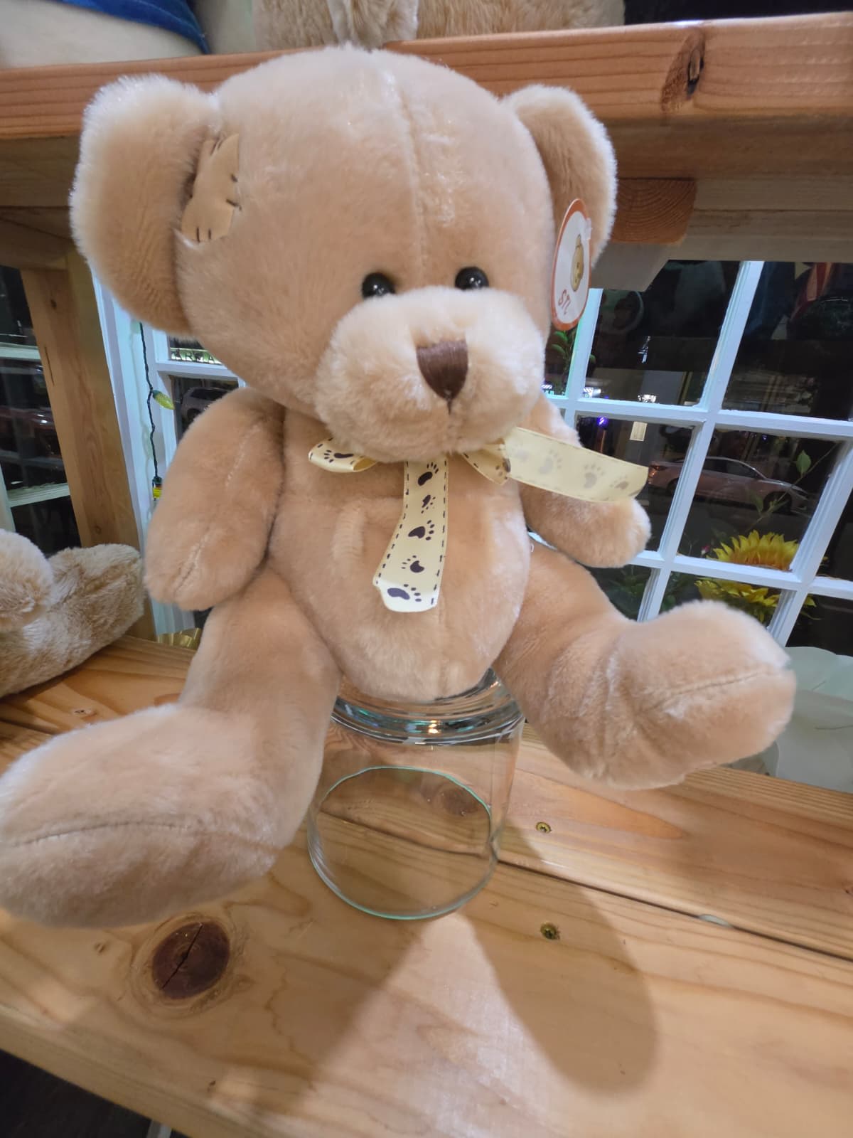 Plush teddy bear with a ribbon bow sitting in a glass jar