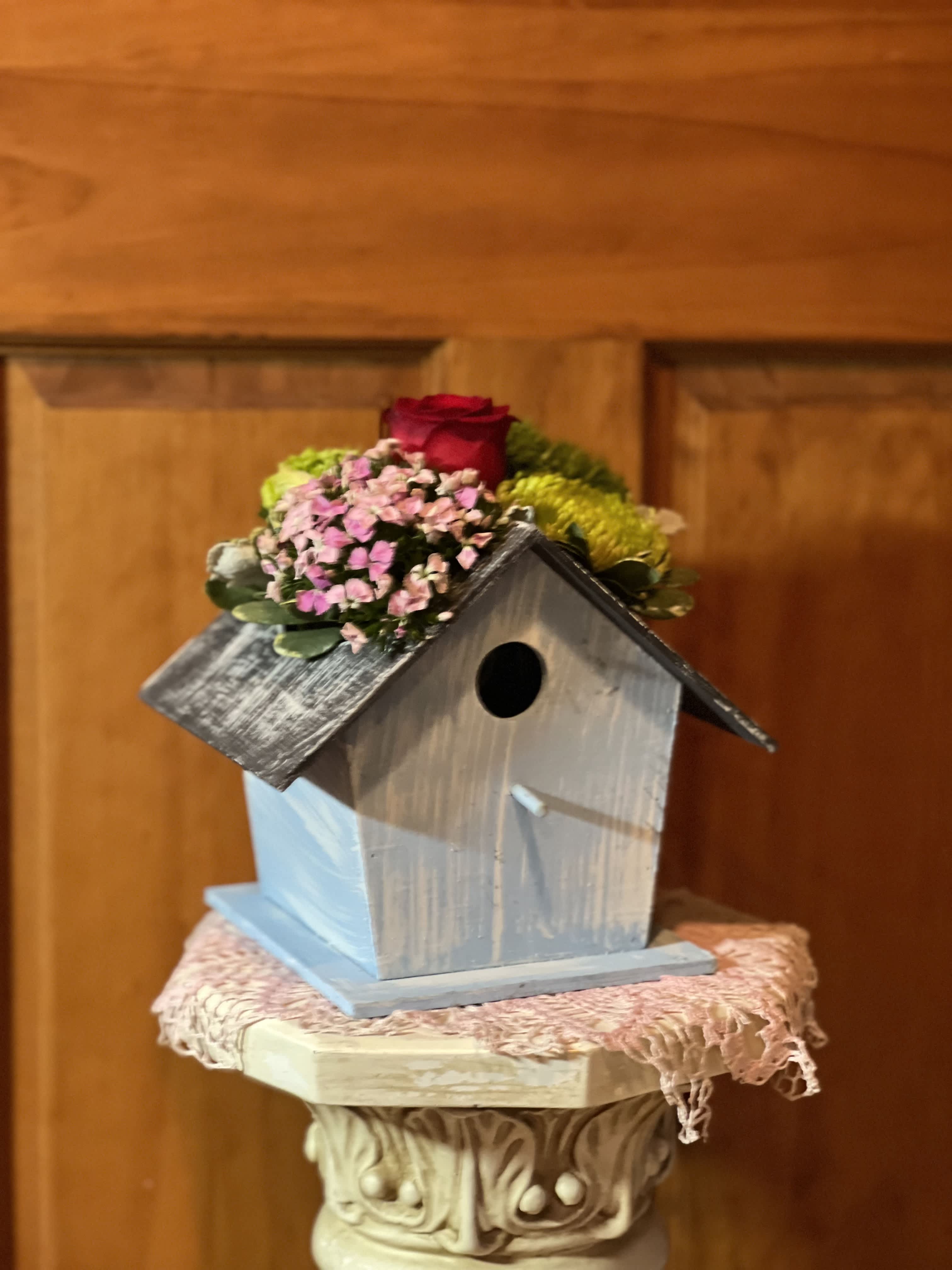 Small birdhouse topped with a red rose and pink flowers
