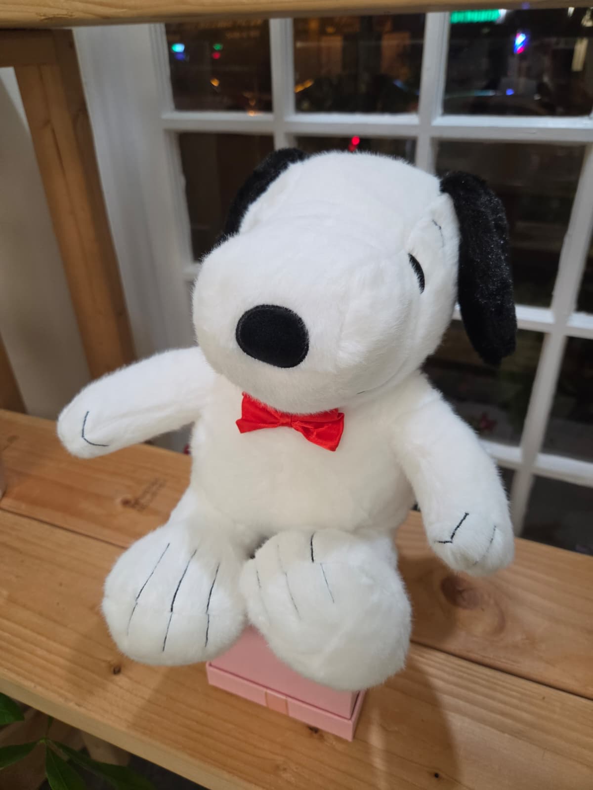 Plush Snoopy toy with a red bow tie sitting on a pink box