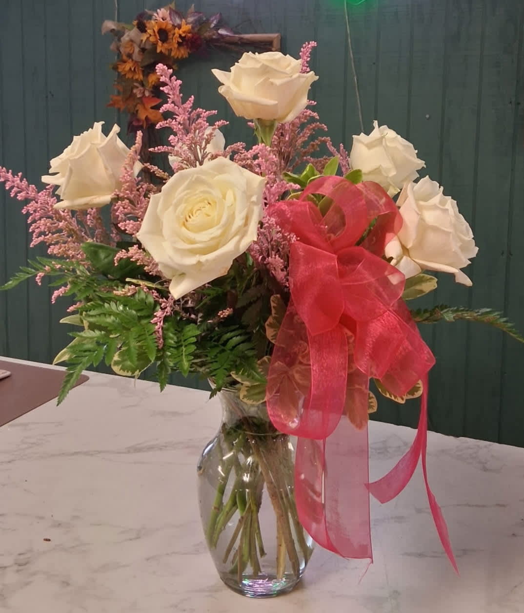 White roses and pink filler flowers in a clear glass vase with a pink ribbon