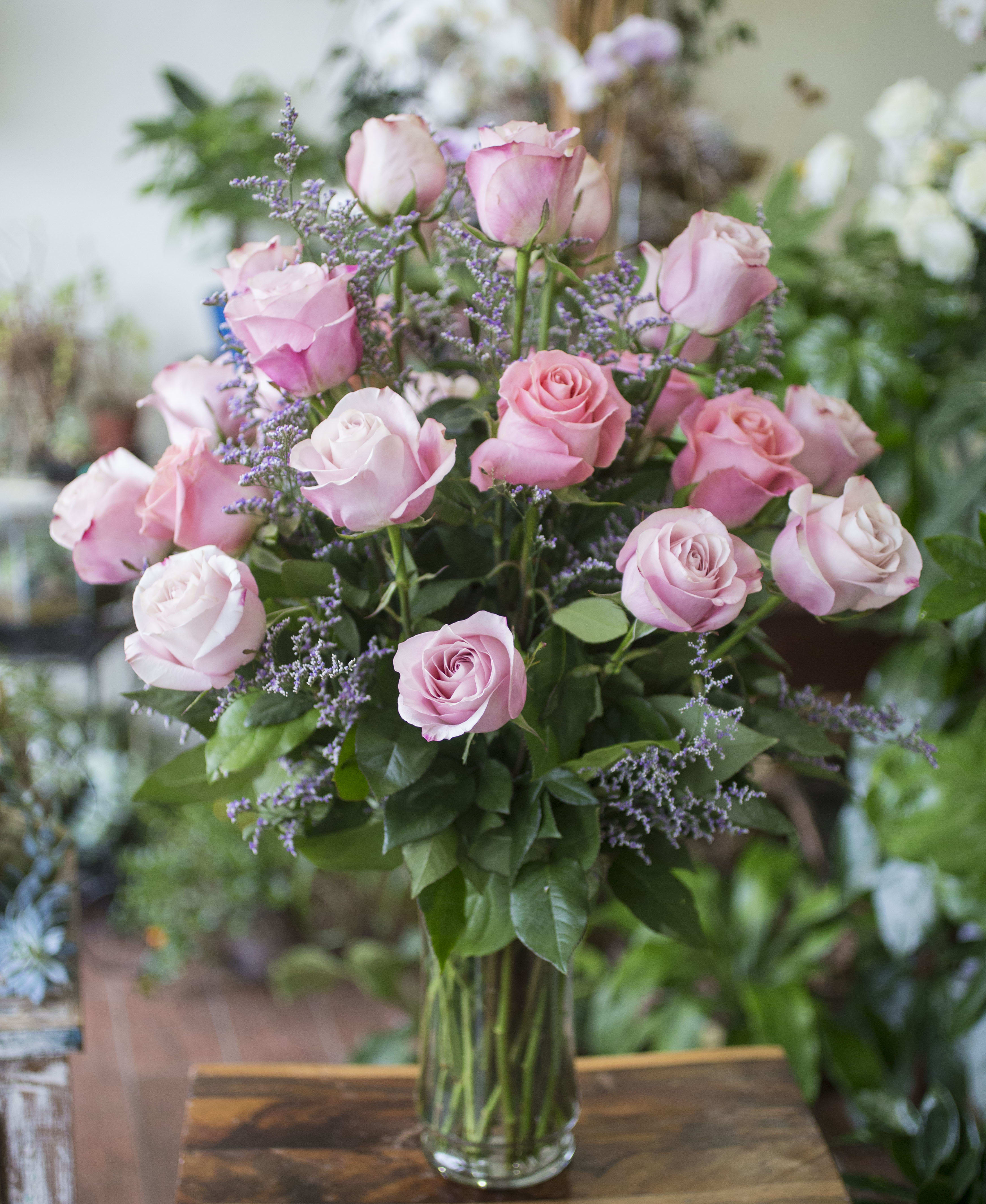 Pink roses arranged in a clear glass vase with purple filler flowers.