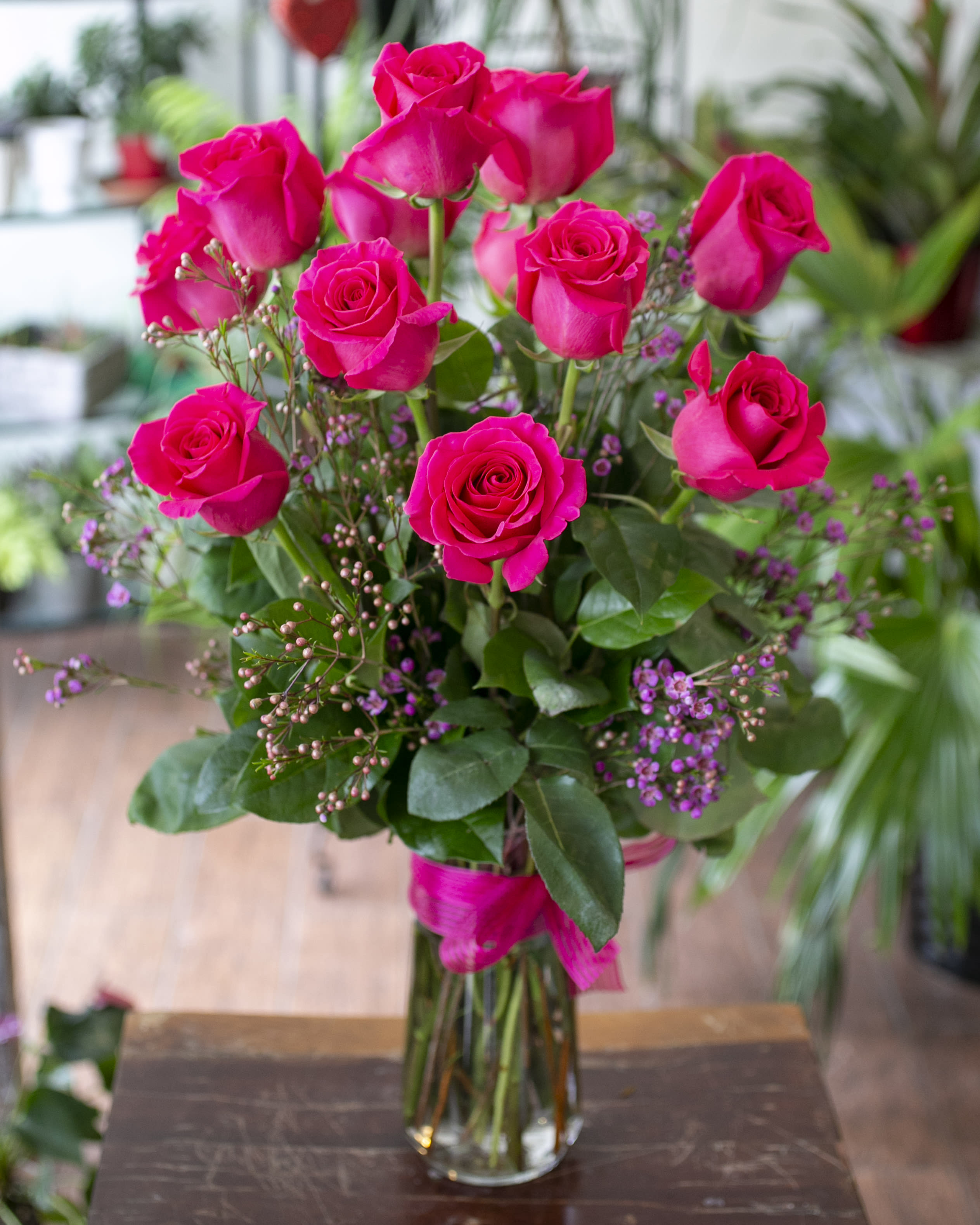 Pink roses arranged in a clear glass vase with small purple filler flowers.