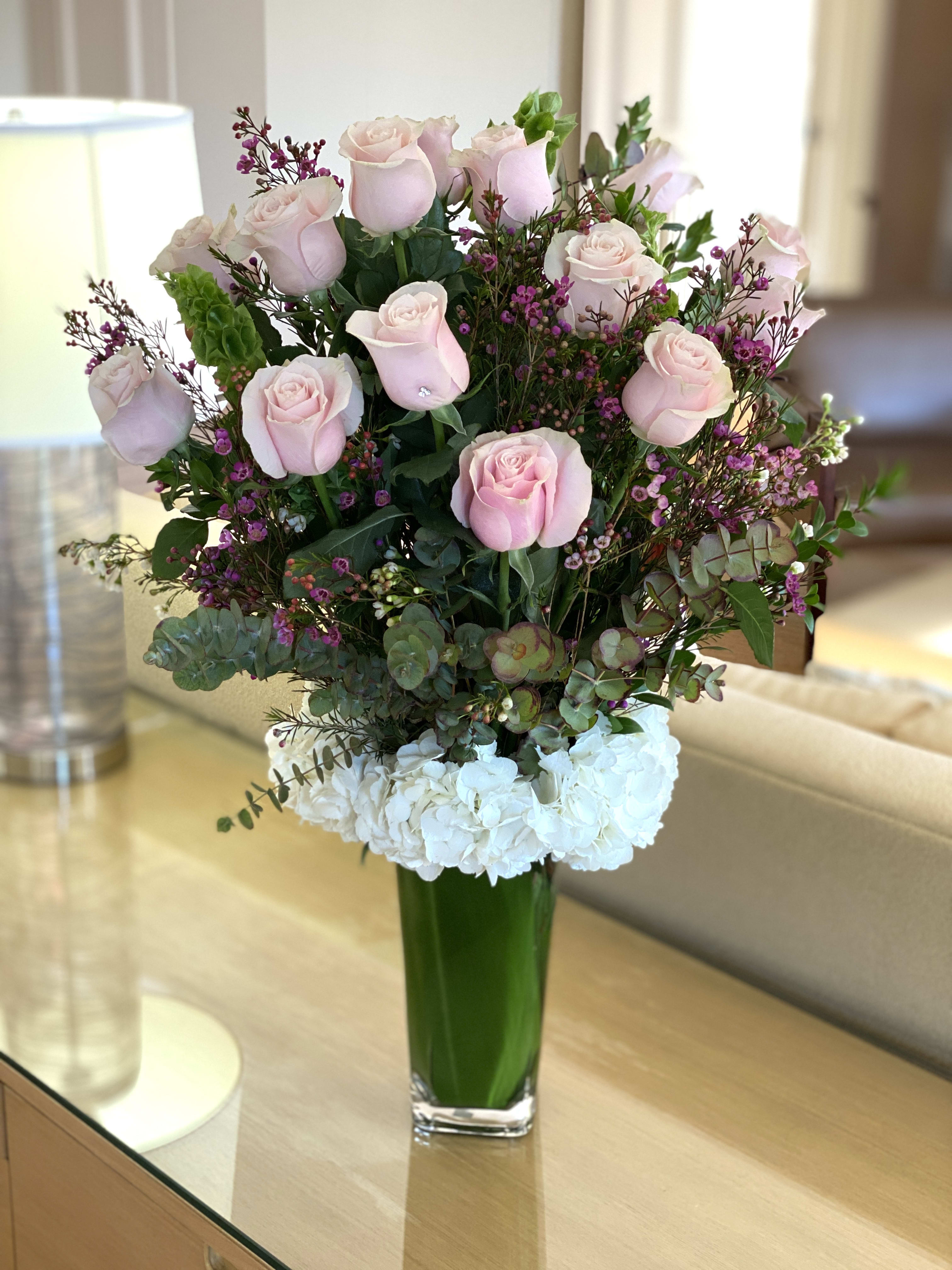 Brooke - Dozen Light Pink Long Stem Roses - Our dozen roses are spectacular, and its no surprise they're one of our most popular item.  Standing tall in a glass vase are 12 long-stem Ecuadorian roses design among lush mixed greens on a bed of hydrangeas. Each one of our arrangements comes with a small butterfly to hold your complimentary greeting card and a small crystal in one of the blooms. 