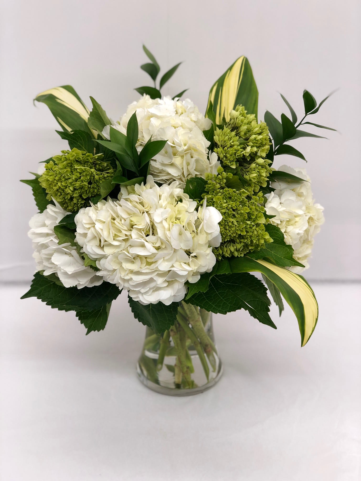 White hydrangea bouquet with green blooms in a clear glass vase