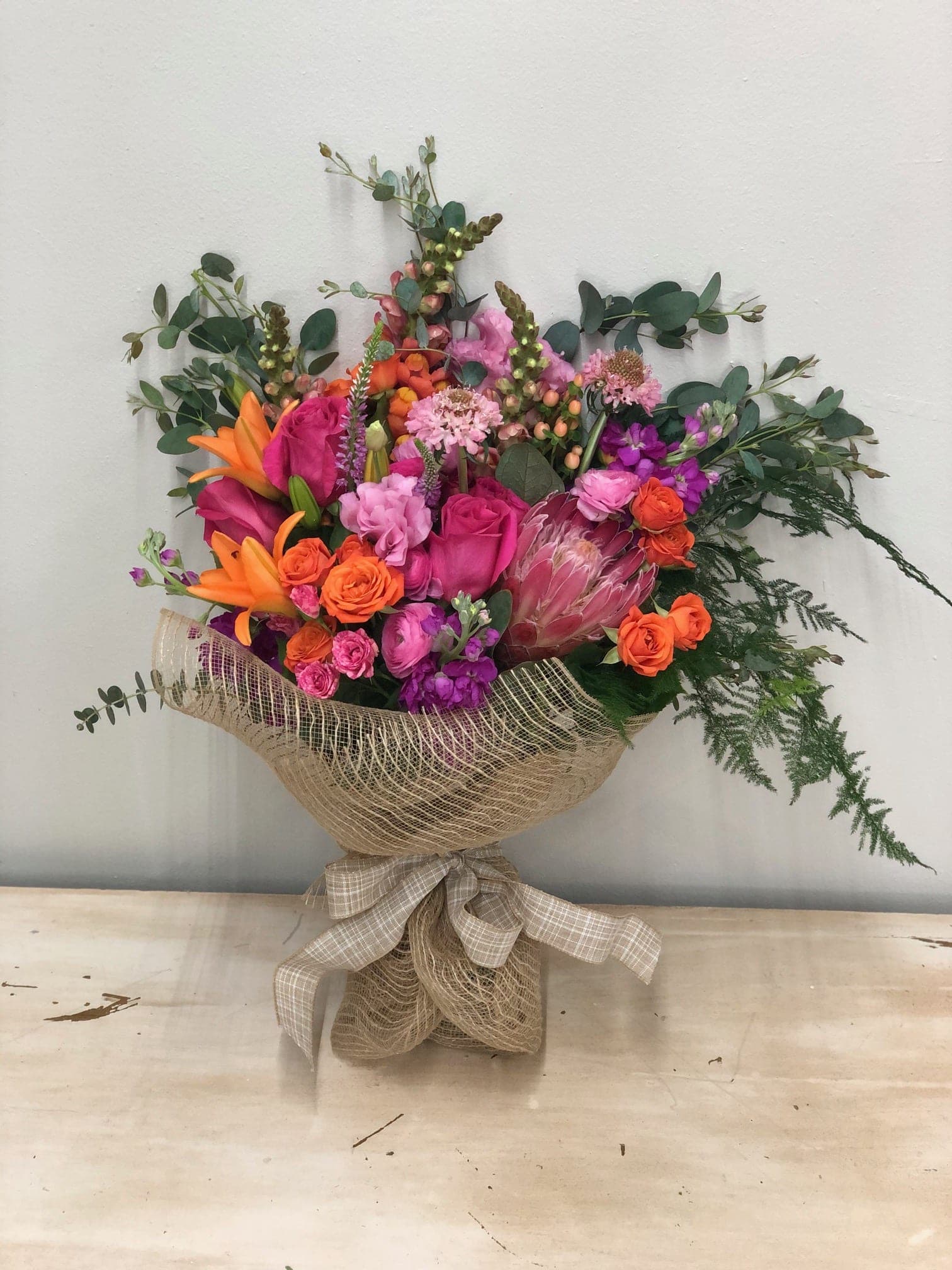 Bright mixed bouquet with pink, orange, and purple flowers wrapped in burlap