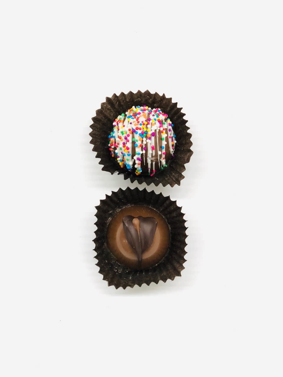 Two decorated chocolate truffles in brown paper cups on a white background