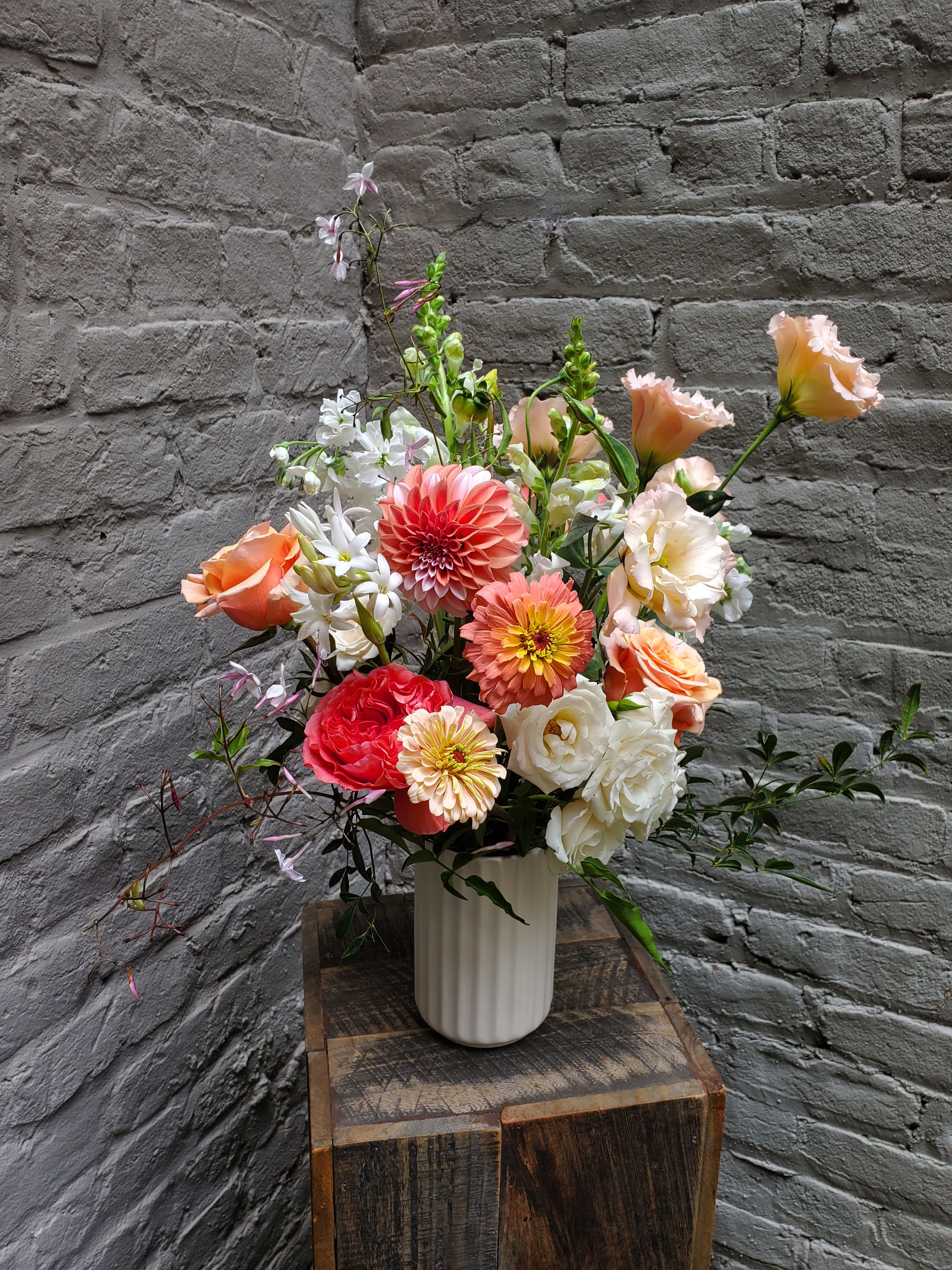 Mixed bouquet of coral, peach, and white flowers in a white vase