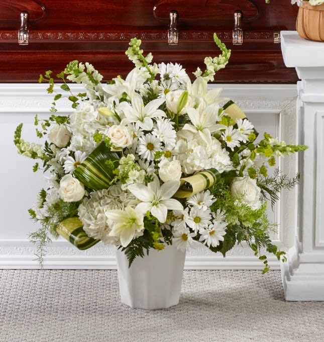 White floral arrangement in a white vase with lilies, roses, and daisies