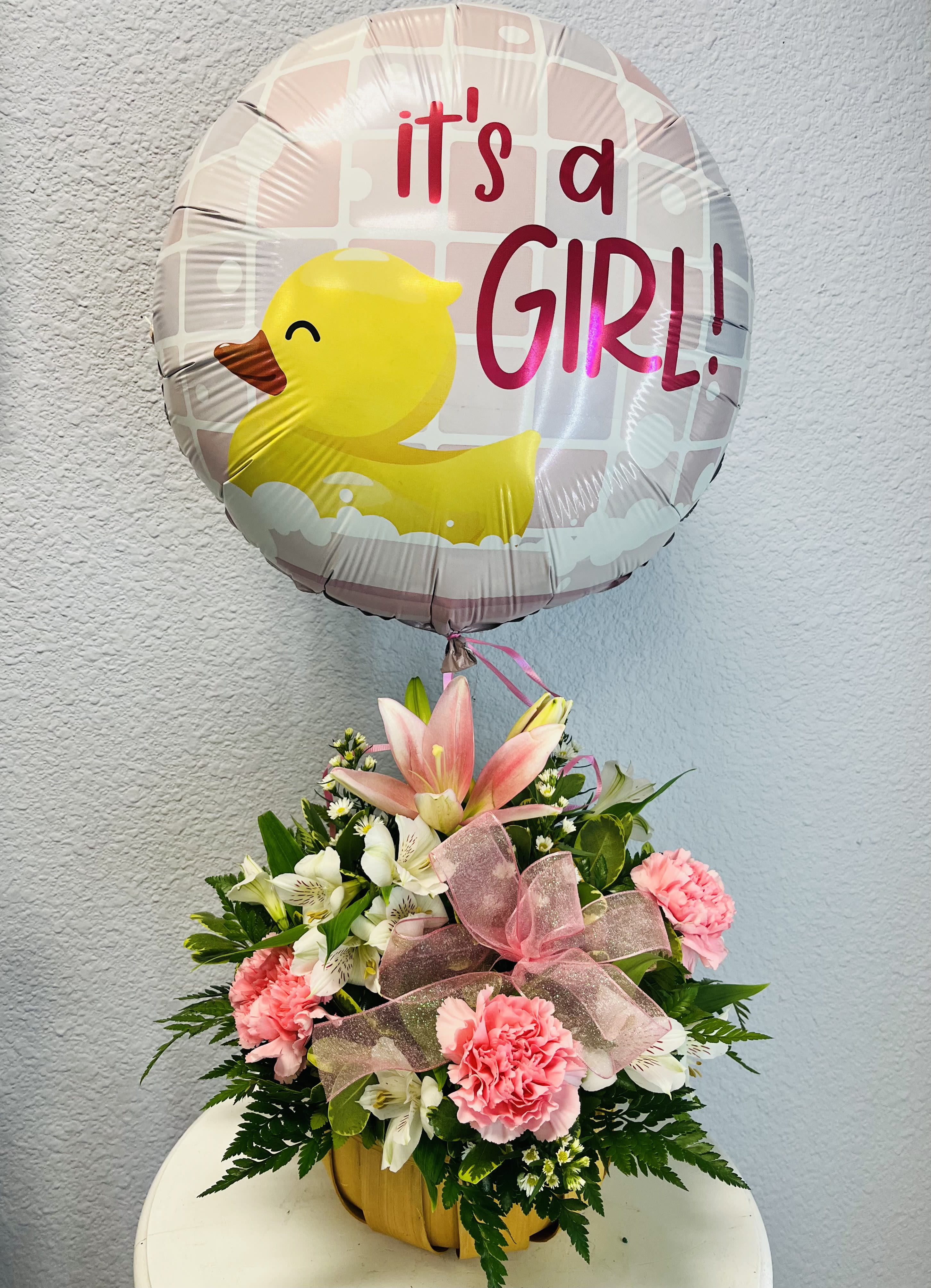 Pink and white flower arrangement with a duck-shaped balloon reading "it's a GIRL!"